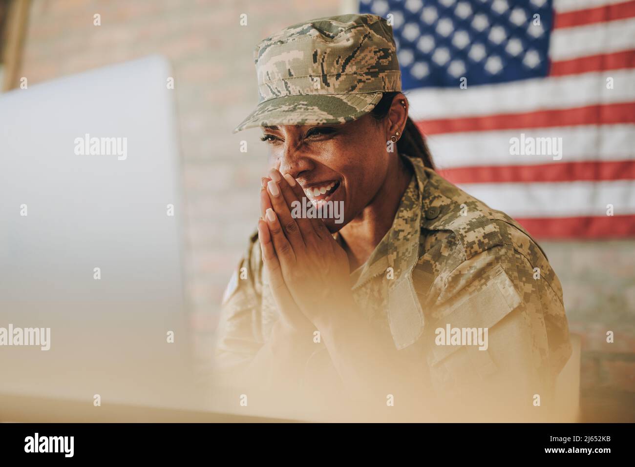 Happy female soldier smiling cheerfully while video calling her family on a laptop. American servicewoman communicating with her loved ones while serv Stock Photo