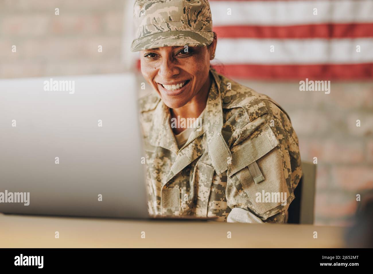 Patriotic female soldier smiling happily while video chatting with her family on a laptop. American servicewoman communicating with her loved ones whi Stock Photo