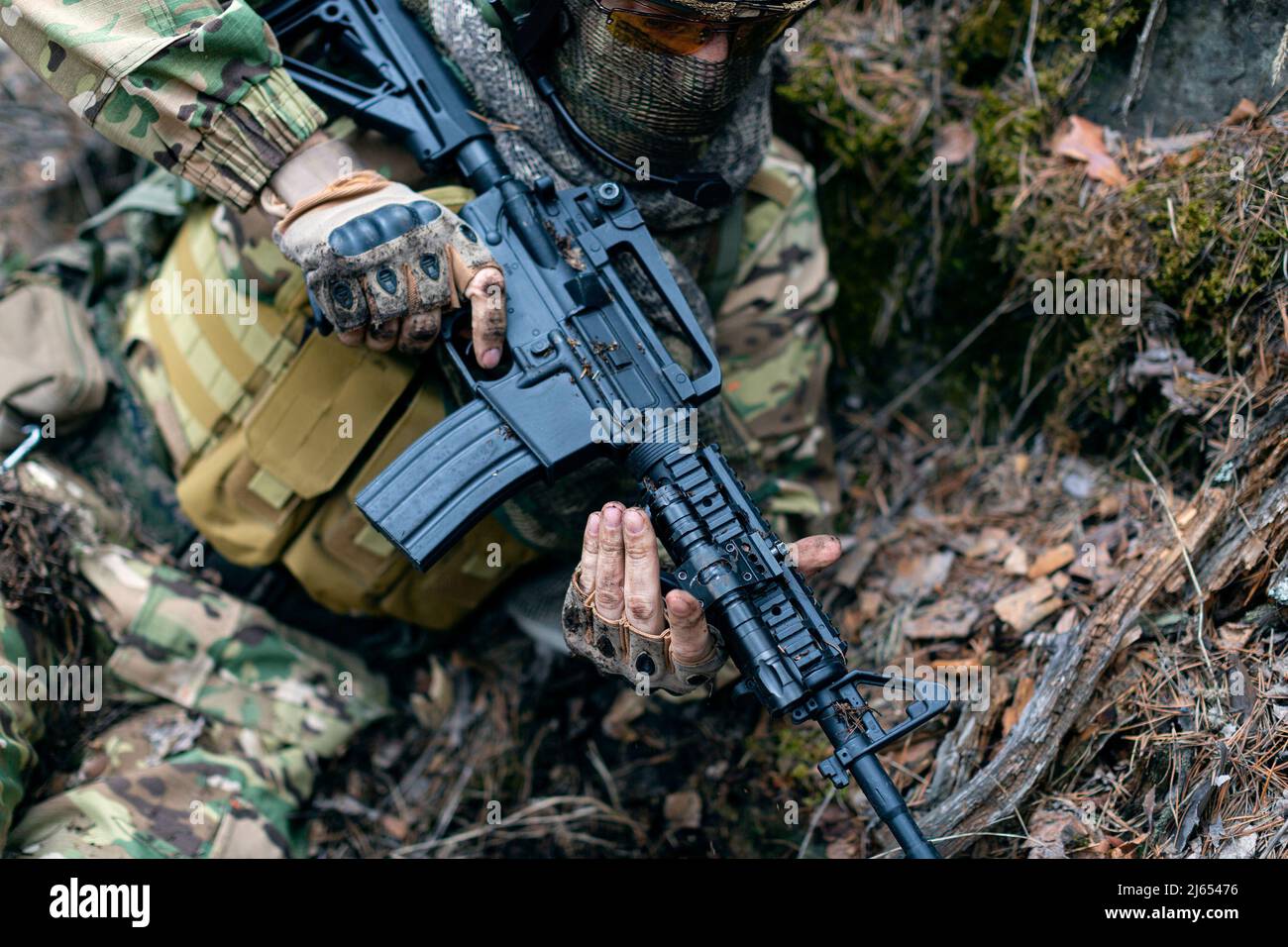 A mercenary soldier in in ambush. He is preparing to attack the enemy. Close-up view. Selective focus on his weapon. Stock Photo