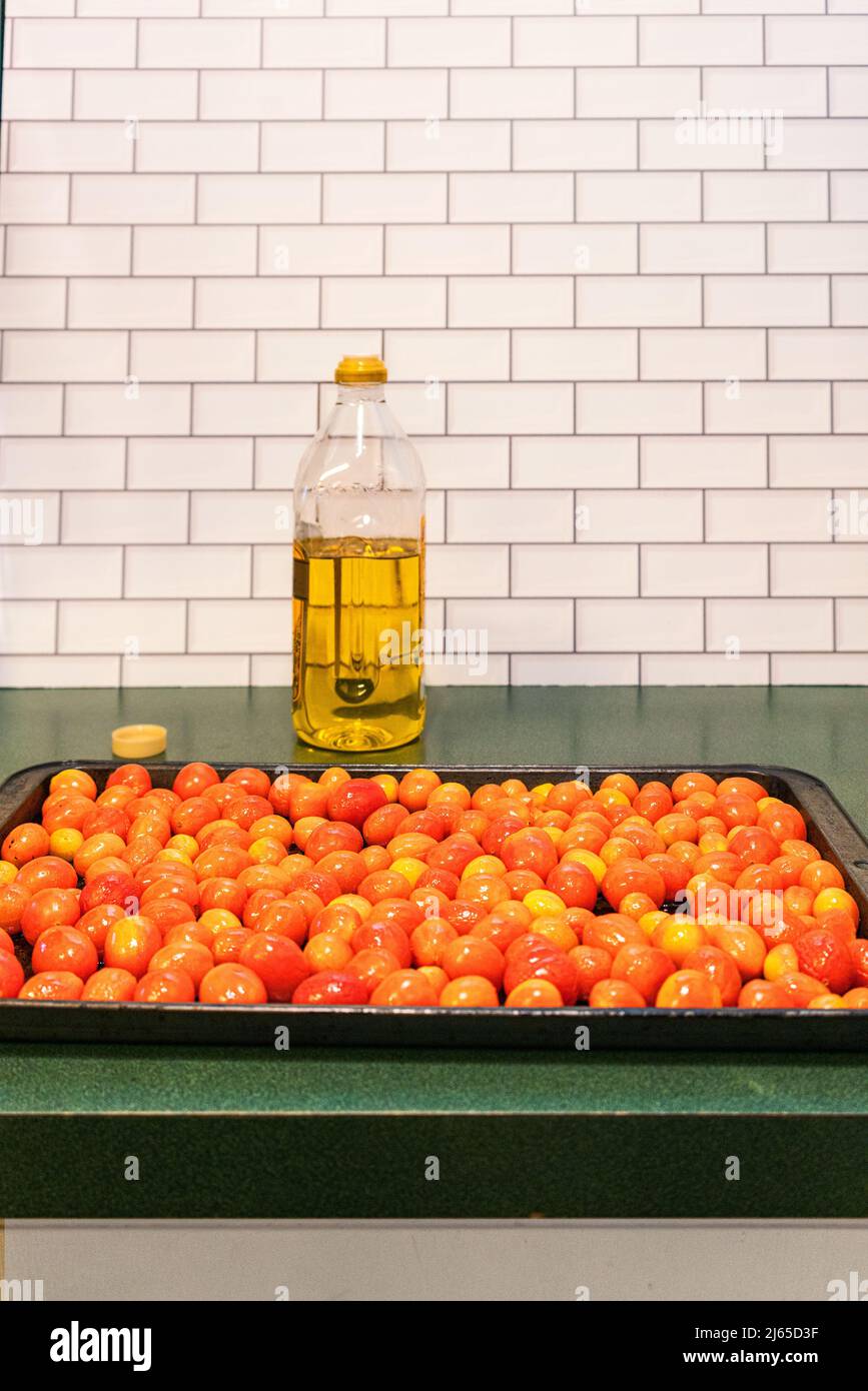 Roasted grape tomatoes on a roasting pan with a bottle of Italian olive oil for fresh pasta sauce.  Healthy Mediterranean diet Stock Photo