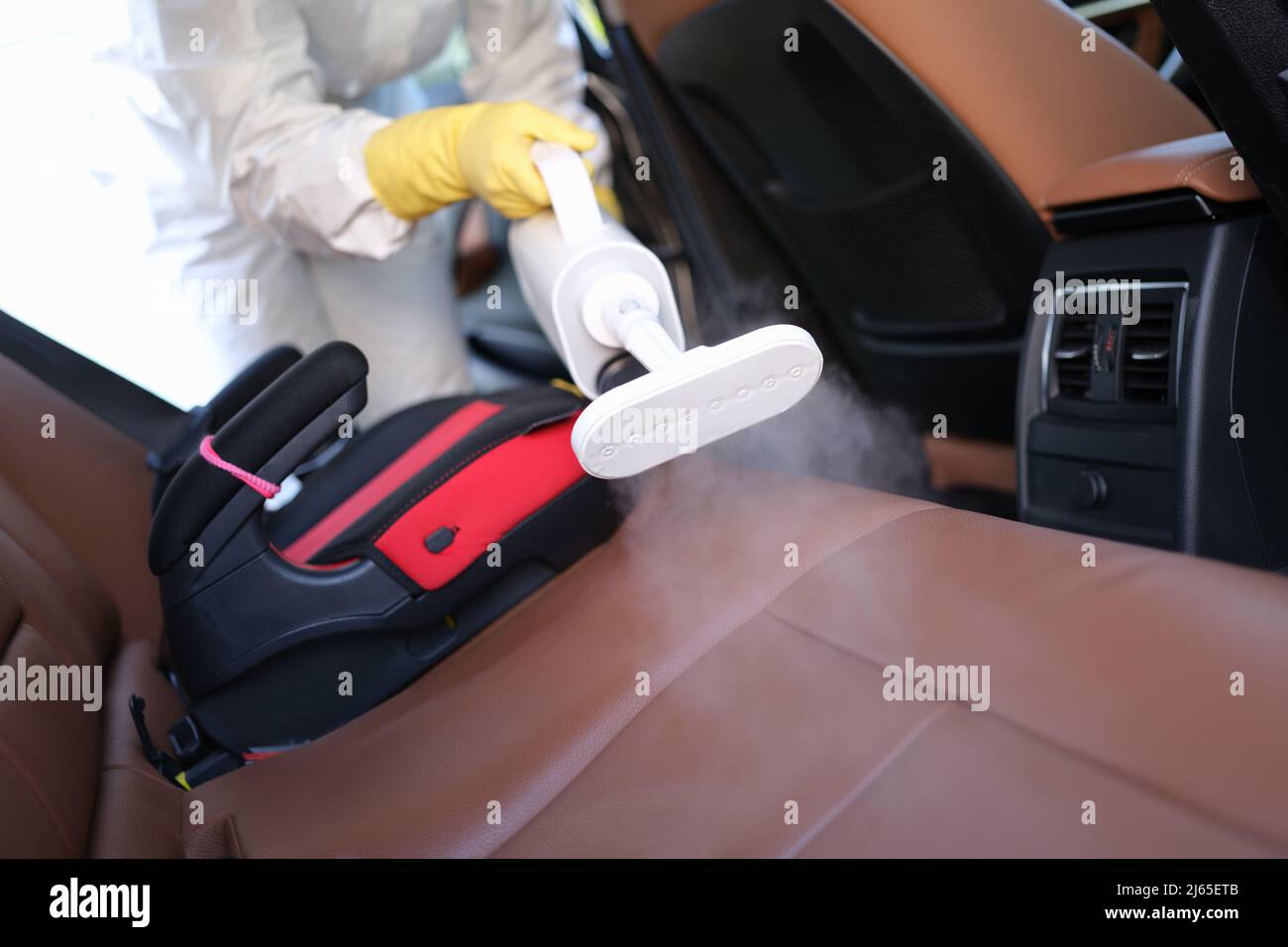 Worker in uniform cleanse car interior using steam cleaner with spray