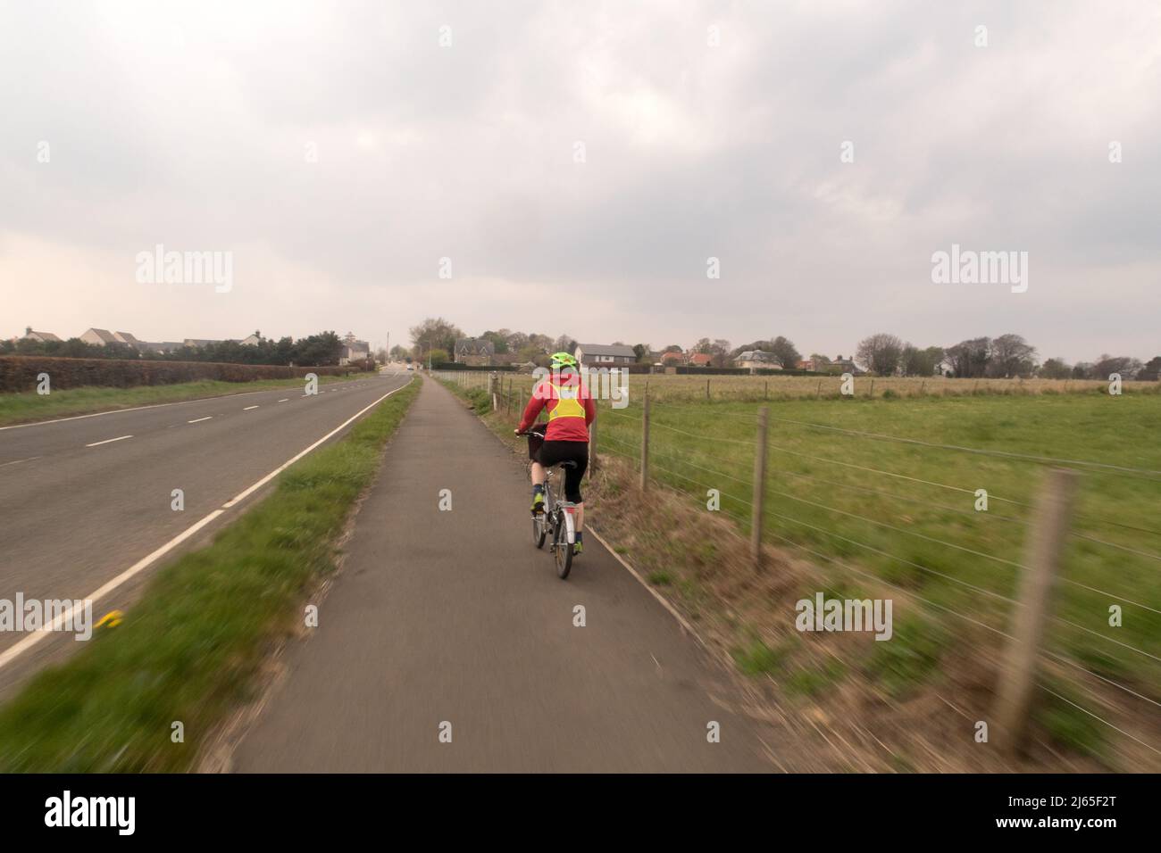 A woman cycling along a cycle path running next to a road in the countryside Stock Photo