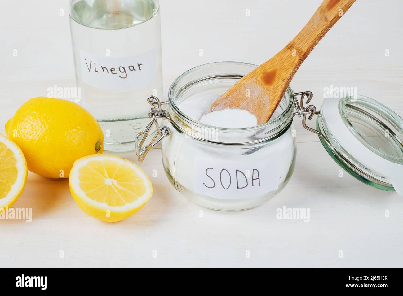 Baking soda in jar, vinegar, lemon, wooden spoon on a white background
