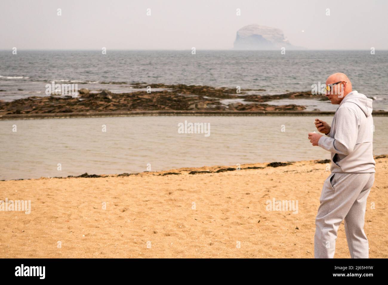 A man eating an ice cream along the beach in North Berwick with the Bass Rock in the background Stock Photo