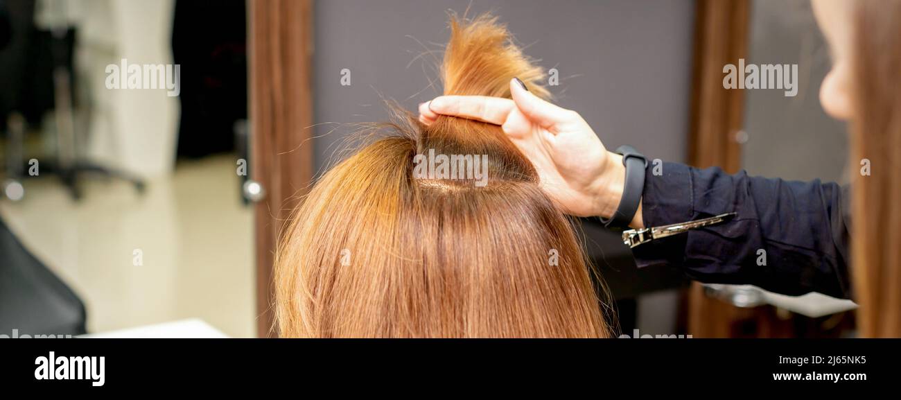 The hairdresser holds a strand in hand between fingers of the female