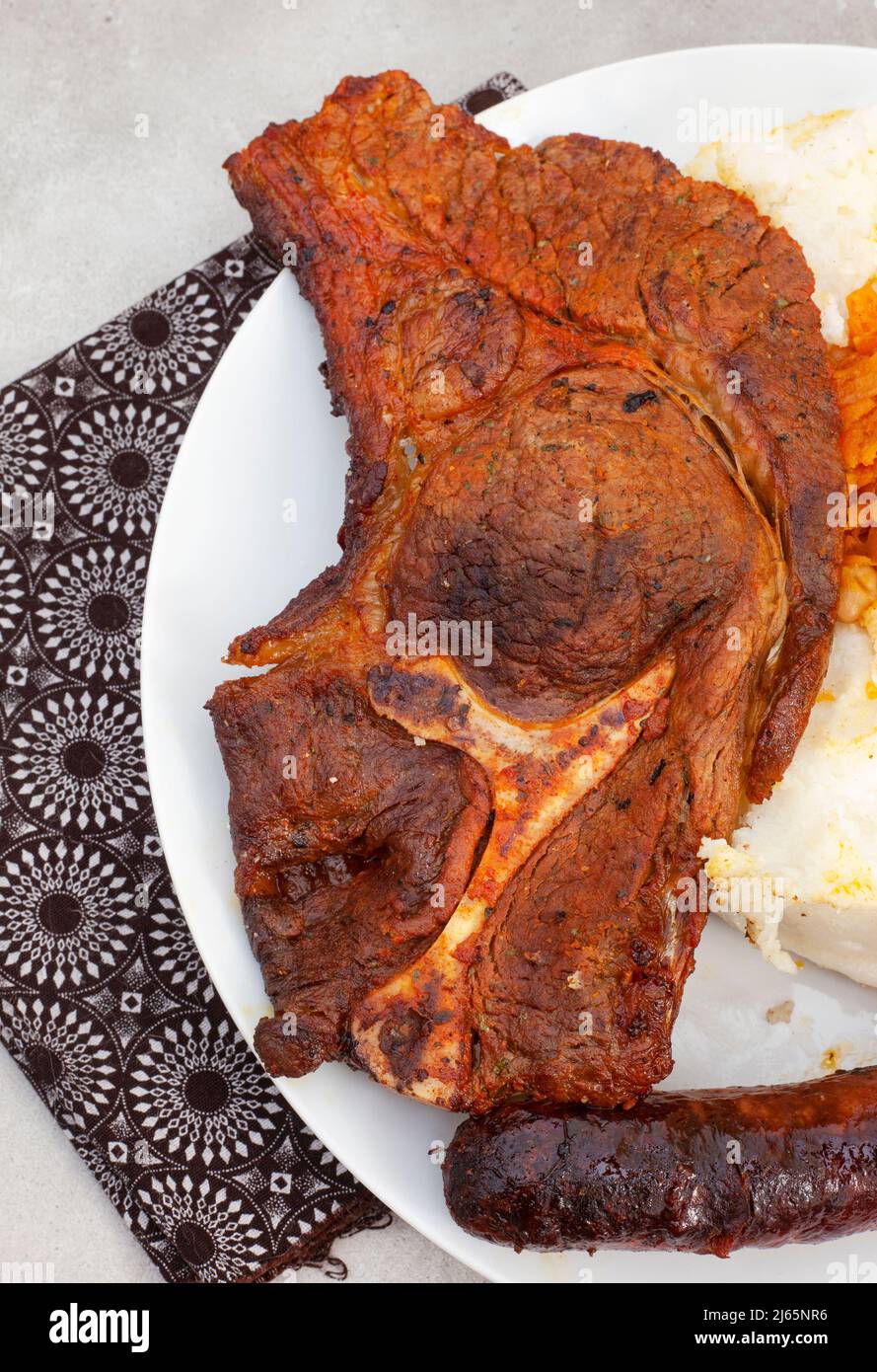 Flat lay of Traditional South African Braai or Shisa nyama, meat cooked on an open flame and traditional side dish of pap and chakalaka. Stock Photo