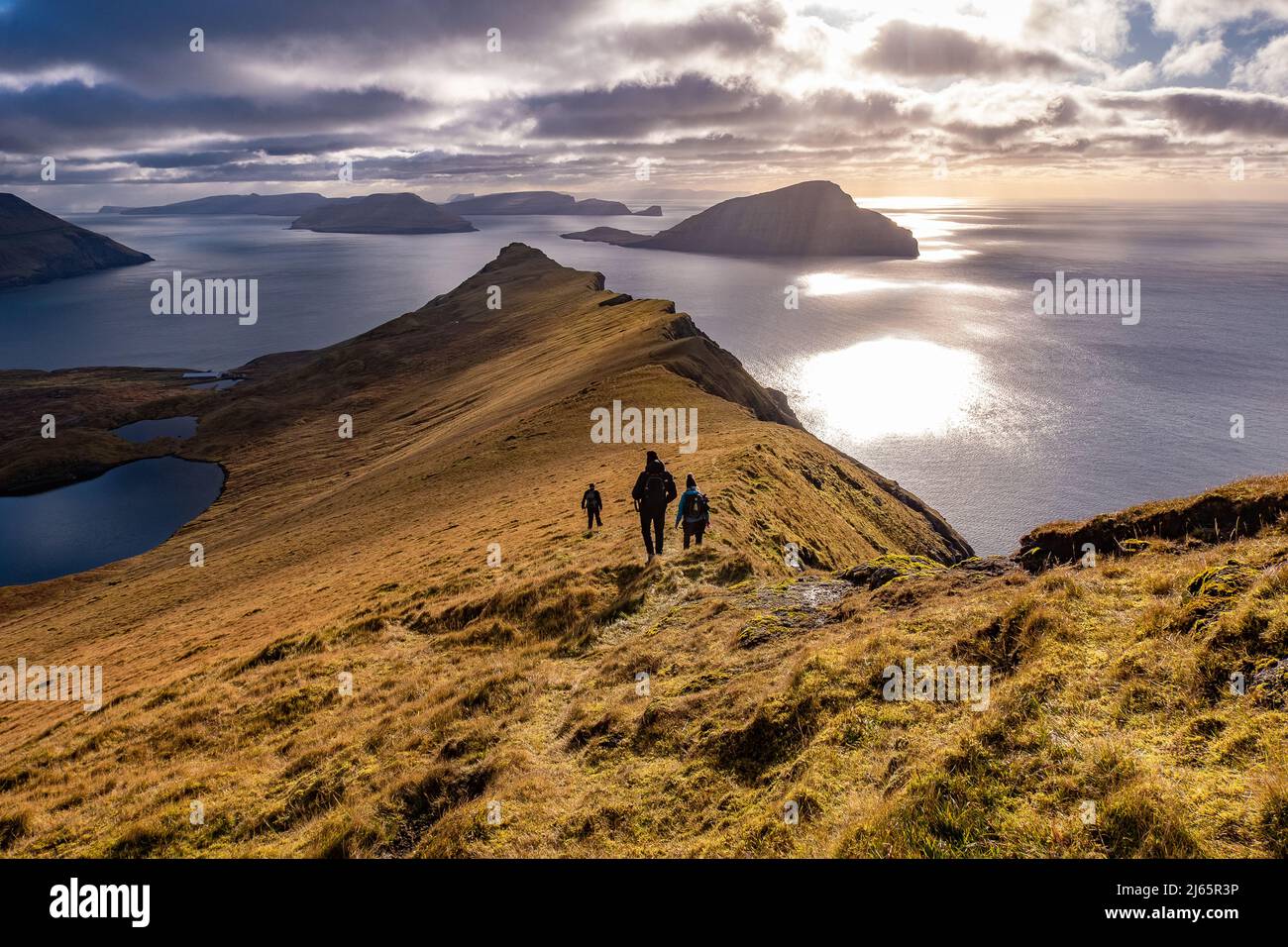 Wandergruppe auf den Färöern,herbstliche Gegenlichtstimmung mit Wolken und Sonne - hiking group on the Faroe Islands Stock Photo