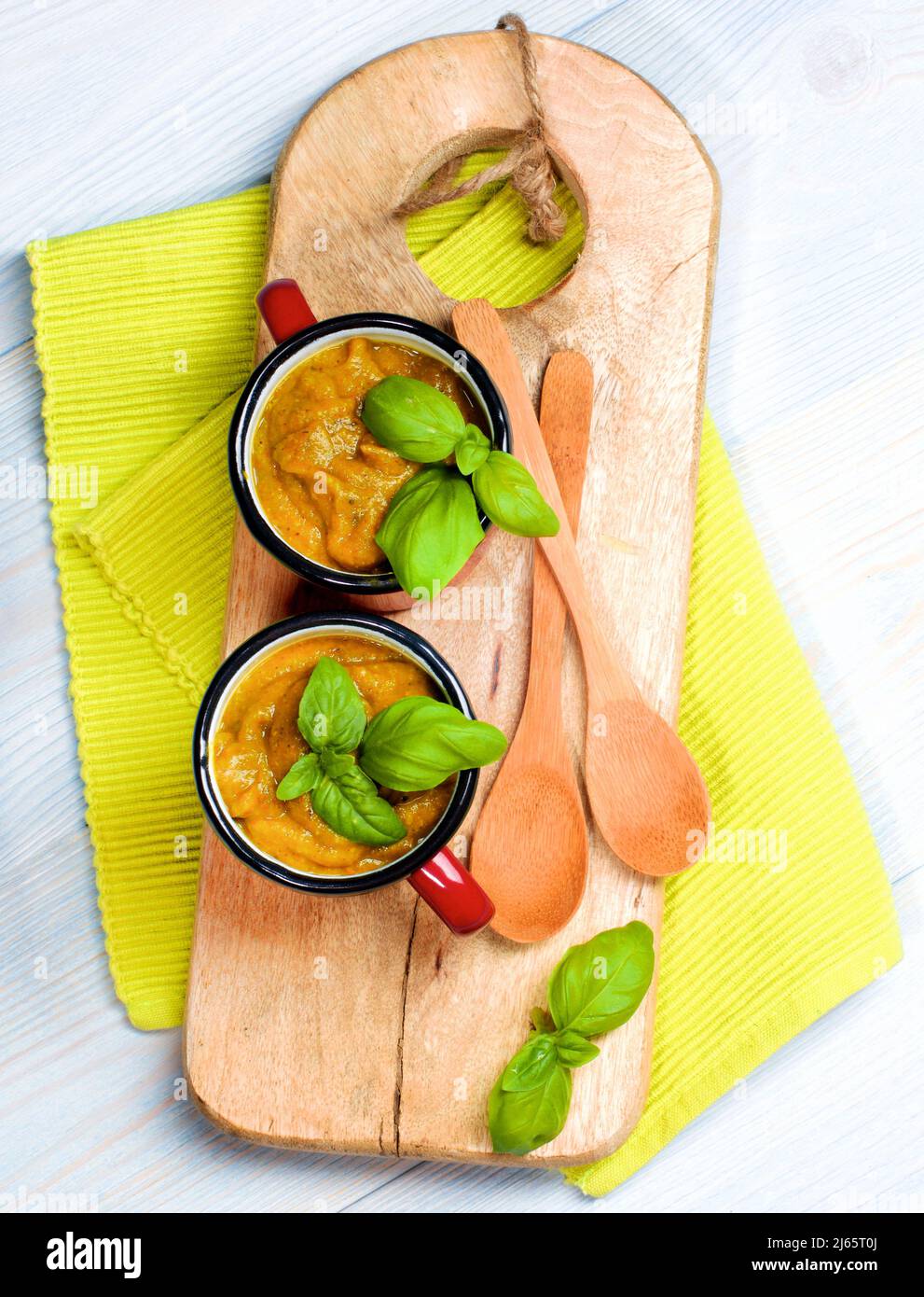 Delicious Vegan Cream Soup in Soup Cups with Wooden Spoons with Basil on Serving Board. Top View Stock Photo