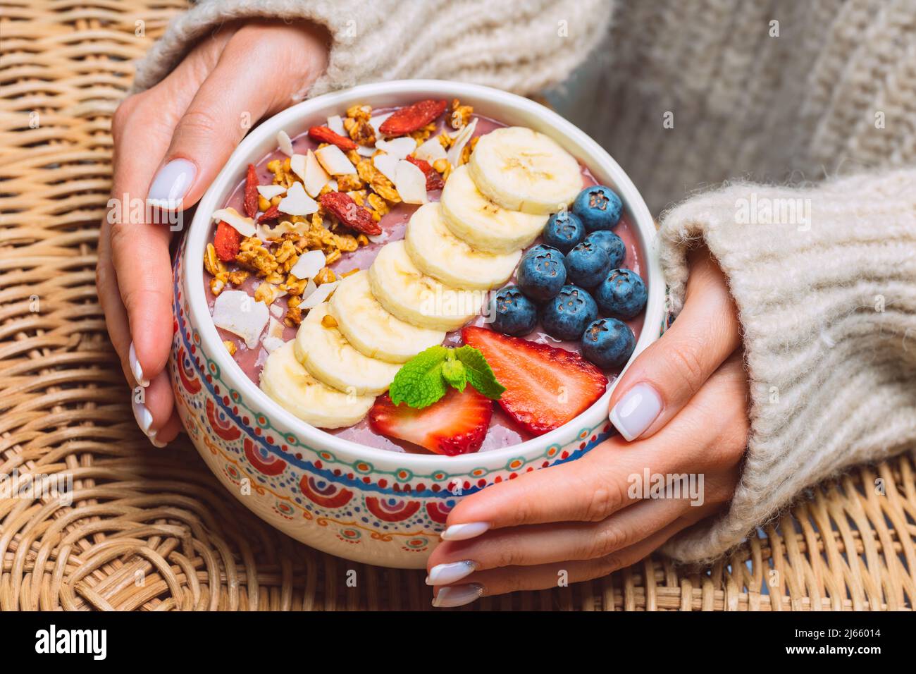 Woman hands holding fresh fruit acai smoothie bowl. Healthy vegan smoothie bowl with banana, strawberry, blueberry and granola. Stock Photo