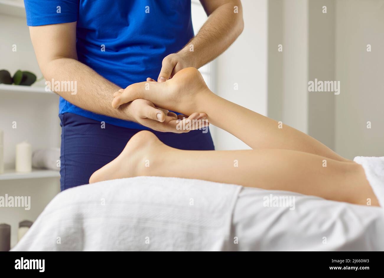 Male masseur therapist doing reflexology foot massage to young woman in modern beauty center. Stock Photo