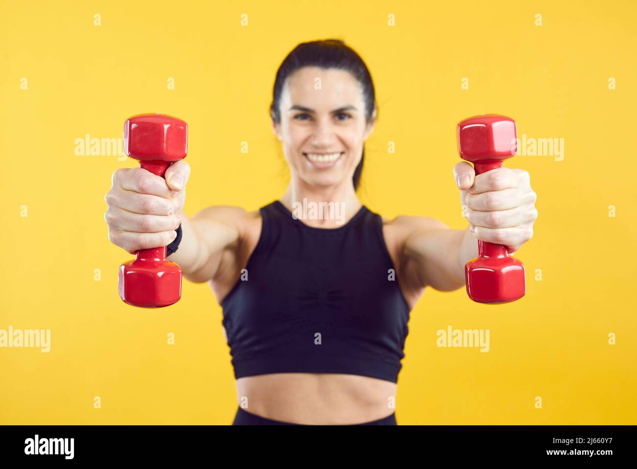 Close up of two red dumbbells in hands of sporty woman isolated on vivid yellow background. Stock Photo