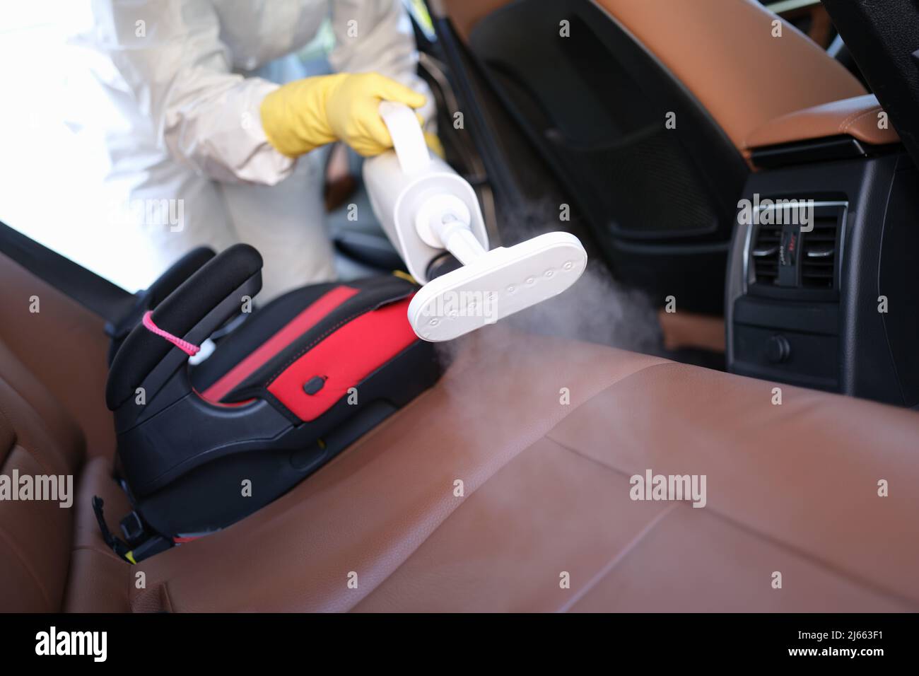 Worker in uniform cleanse car interior using steam cleaner with spray
