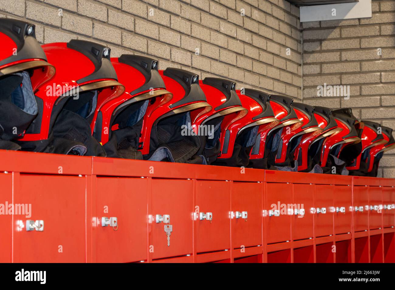 Red fire helmets placed in a row, on top of the fire brigade wardrobes. Ready to fight a fire or calamity Stock Photo