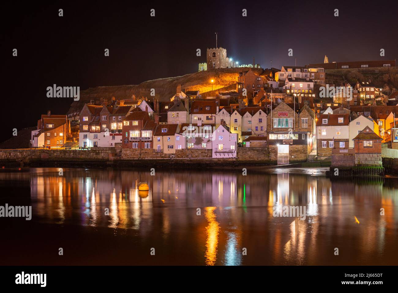 The light of Whitby old town reflected in the calm waters of the harbour Stock Photo