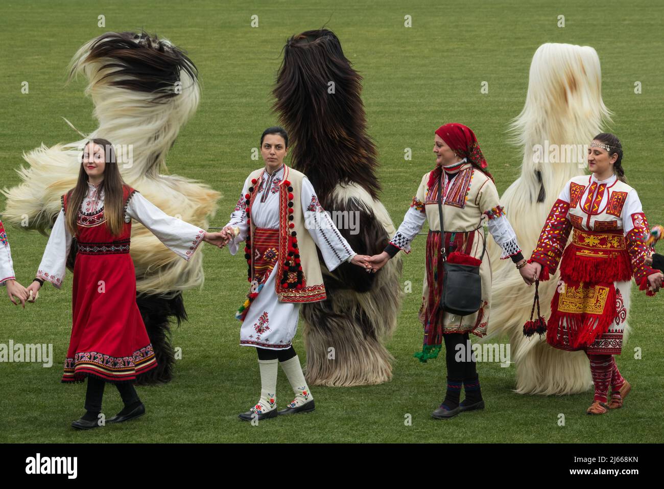Bulgarian Mummers (Kukeri) and womens in traditional Bulgarian costumes dancing at 'Simitli - ancient land of mummers' Stock Photo
