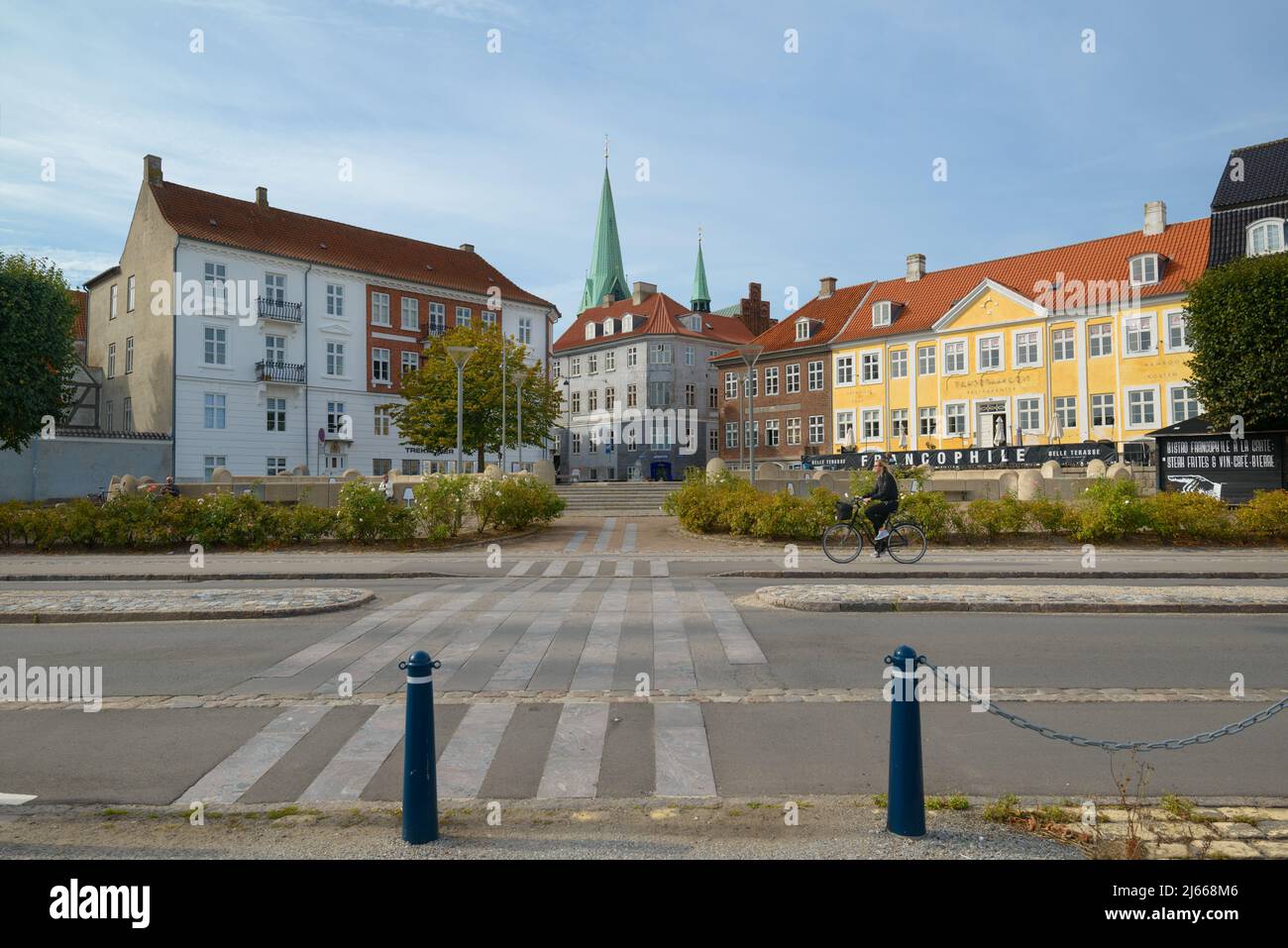 Helsingør, Denmark / 09.22.2016: View of a coastal street in Helsingør, a girl riding a bike, resting people in a small park area, old buildings and a Stock Photo