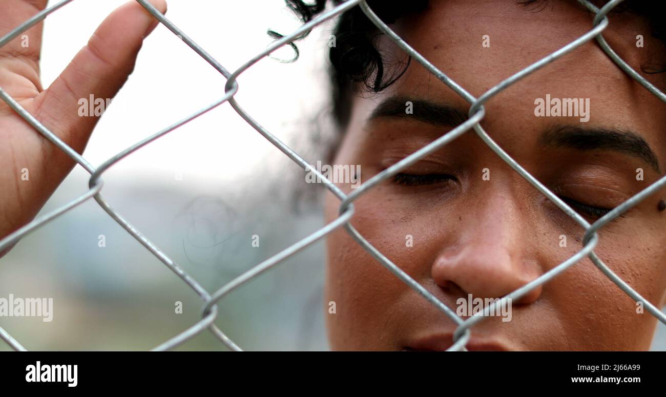 Sad African American woman looking through metal fence. South American person holding into fence Stock Photo