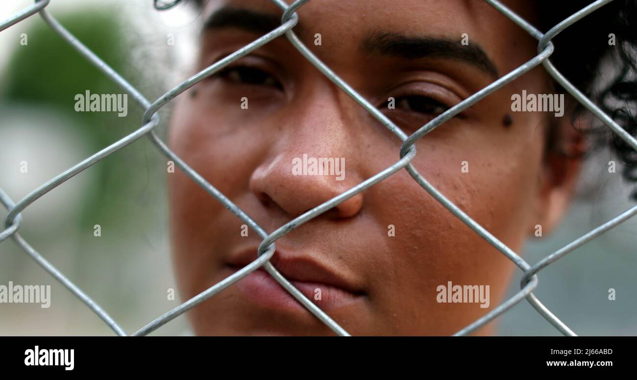 Sad African American woman looking through metal fence. South American person holding into fence Stock Photo