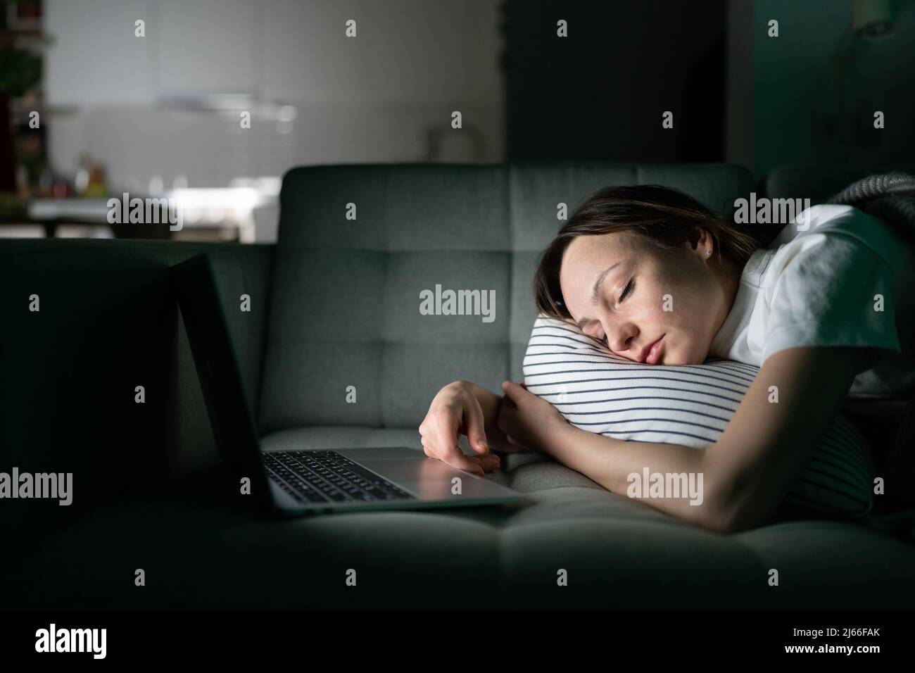 Exhausted young woman sleeping on couch after working with laptop
