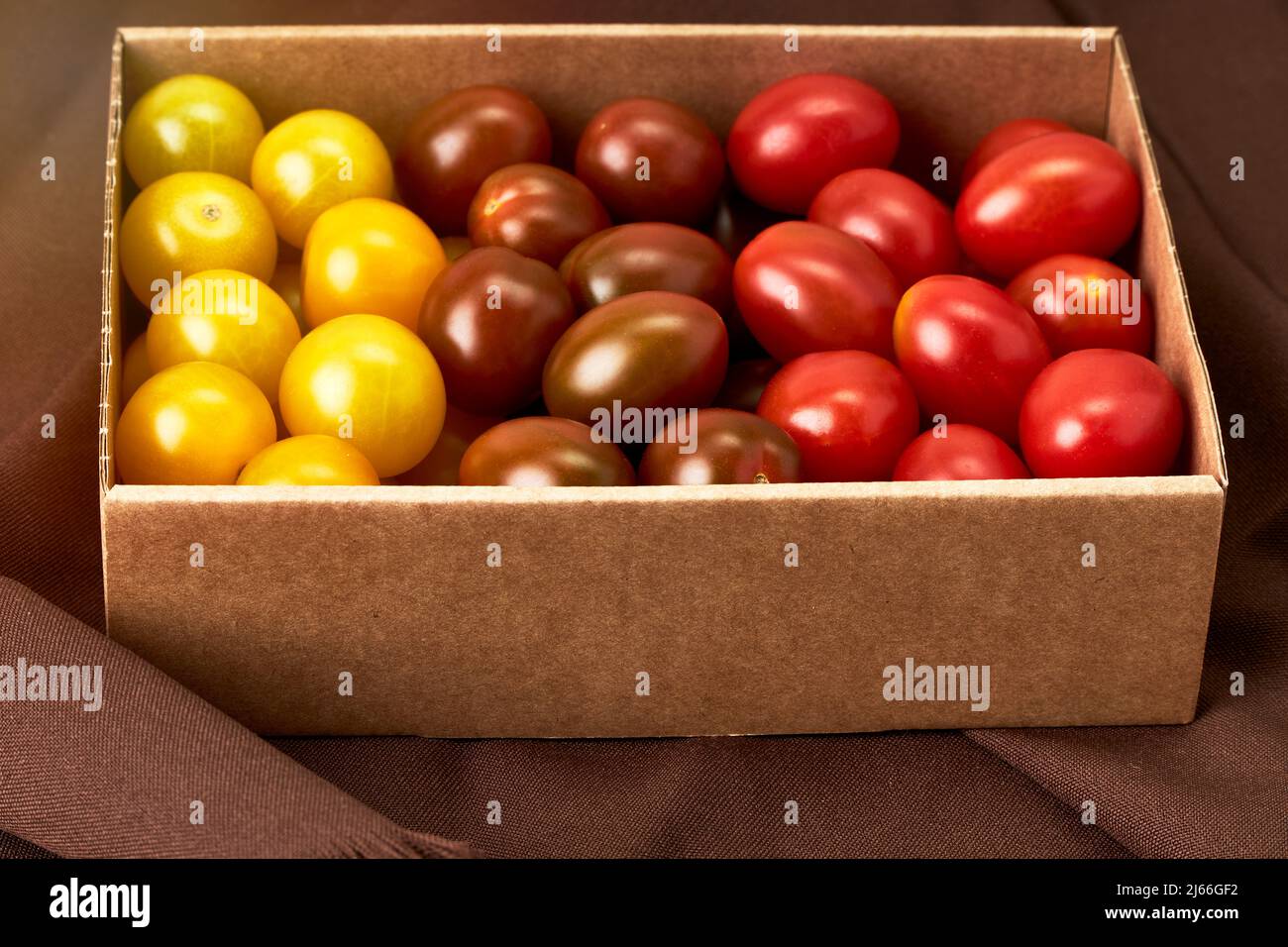 Cardboard box with cherry tomatoes of various colors on a brown cloth