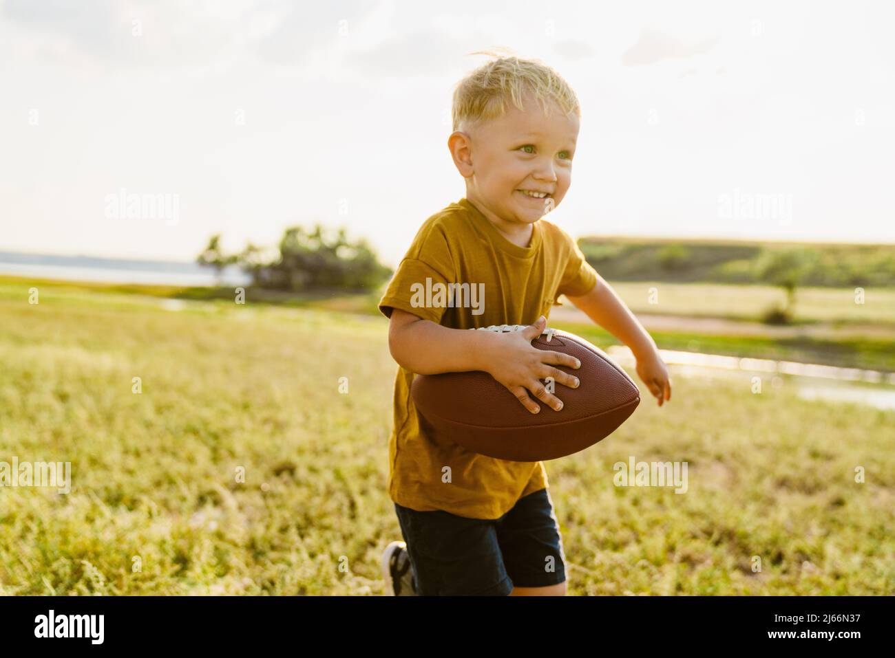 Blonde white boy smiling while playing with rugby ball outdoors Stock ...
