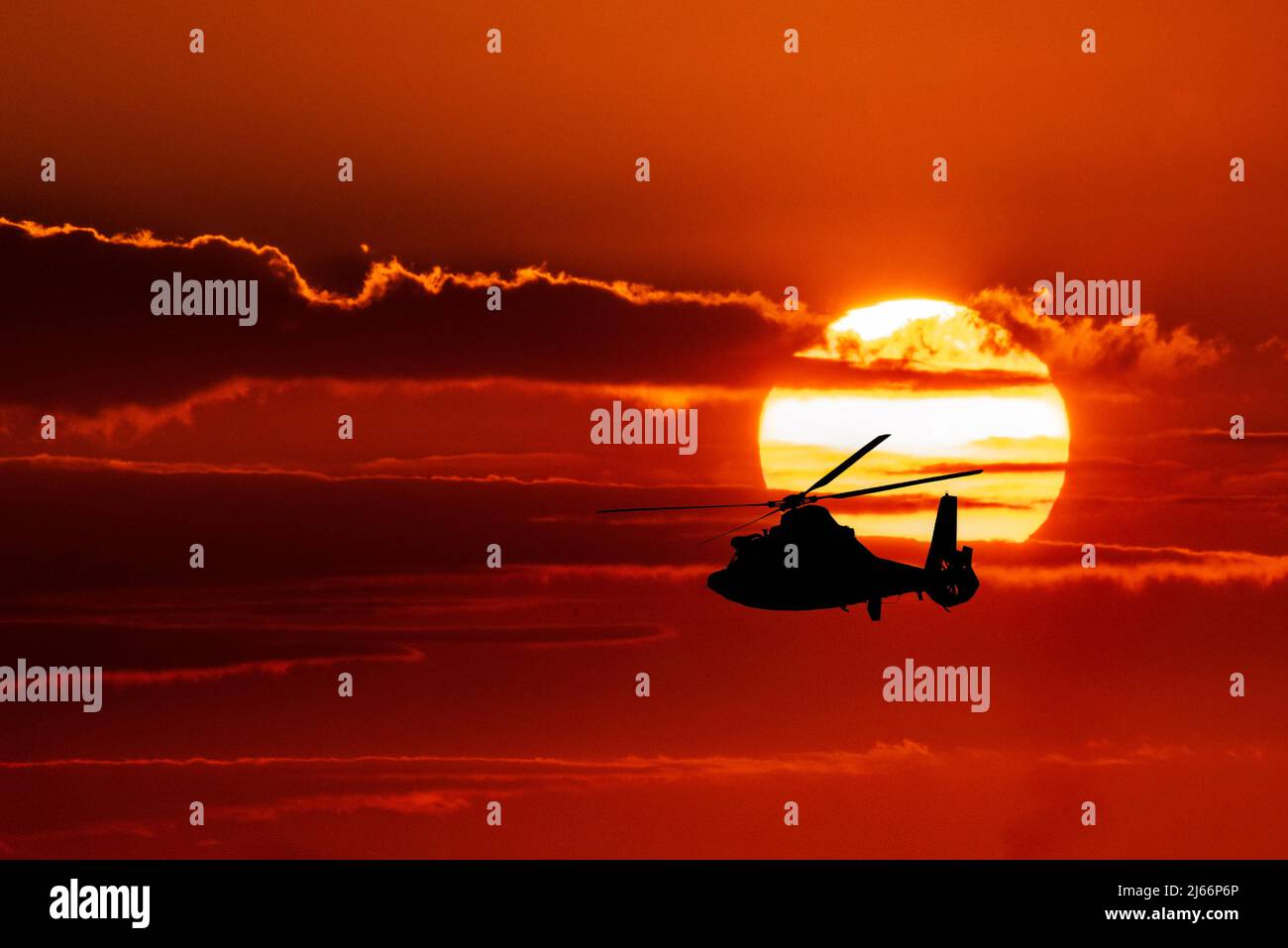 A U.S. Coast Guard helicopter flies in silhouette against the setting ...