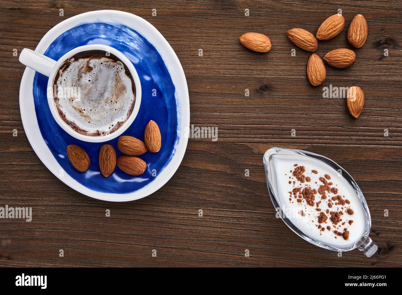 Cup of cappuccino almonds and milk in a glass milk jug on a dark wooden table Stock Photo
