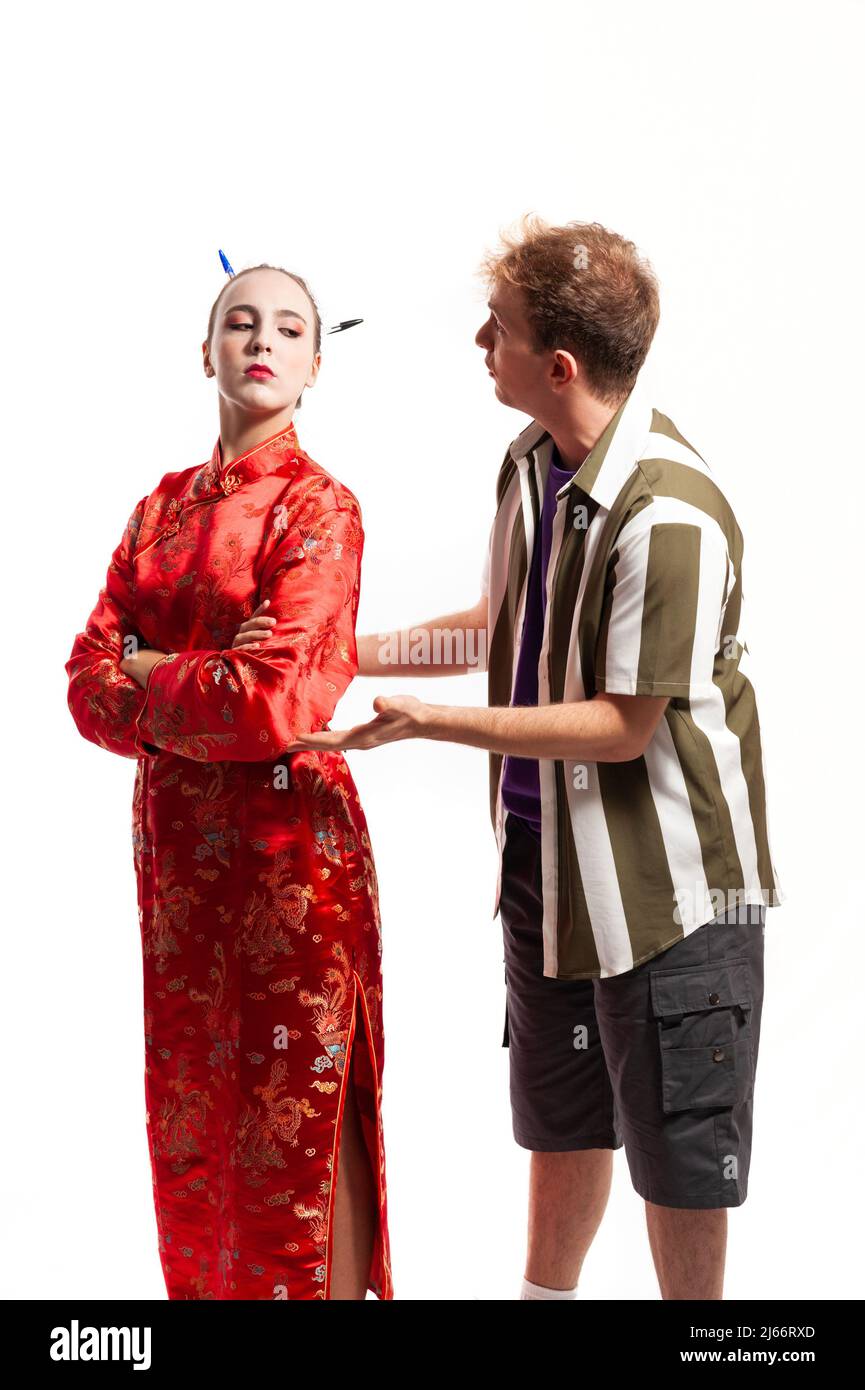 multiethnic couple, male and female. Woman dressed in traditional red Chinese costume looking over her shoulder and man dressed in shirt pleading and Stock Photo
