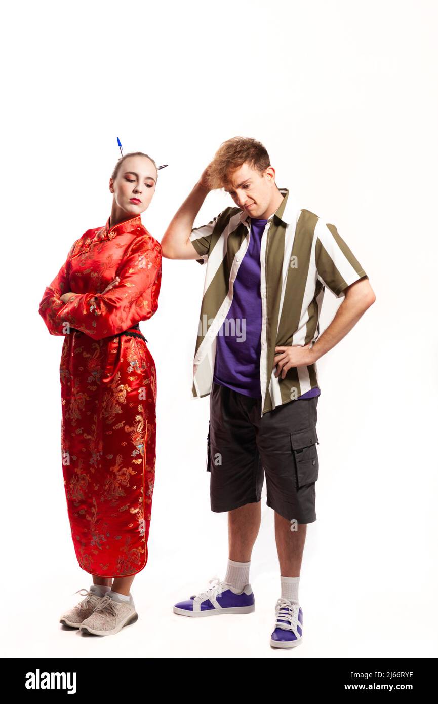 multiethnic couple, male and female. Woman dressed in traditional Chinese red dress looking over her shoulder and man dressed in shirt thinking scratc Stock Photo
