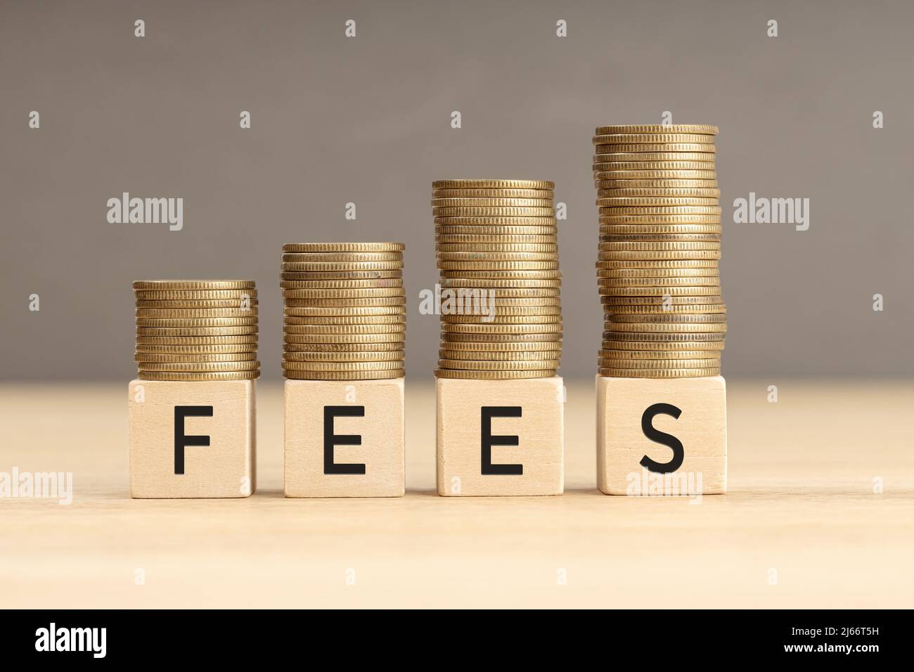 Fees word in wooden blocks with coins stacked in increasing stacks. Fees increasing concept. Copy space Stock Photo