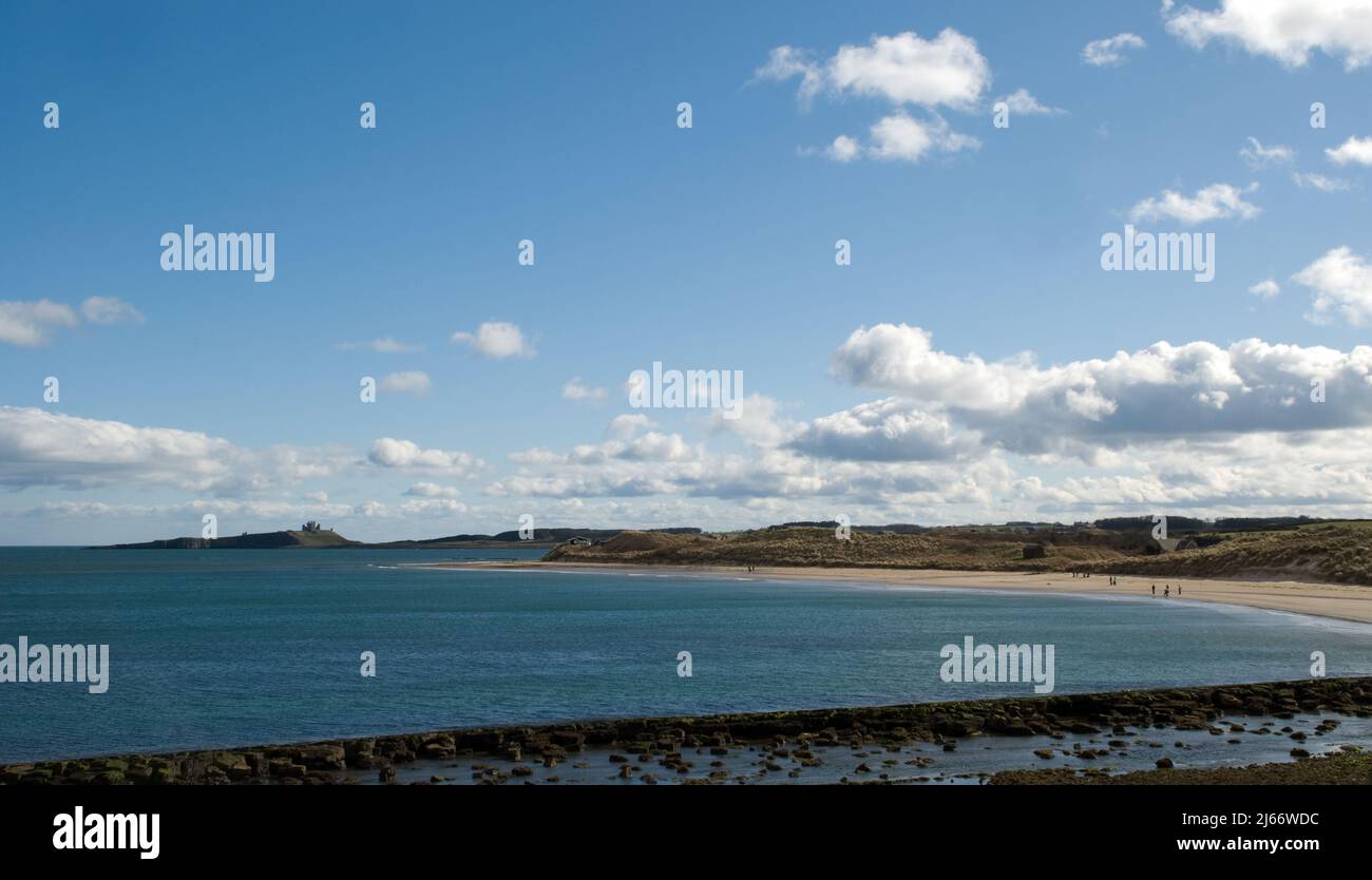 Landscape of a wide sweeping view of a curving coastline and bays towards a distant Dunstanburgh Castle on the skyline seen from Low Newton Stock Photo