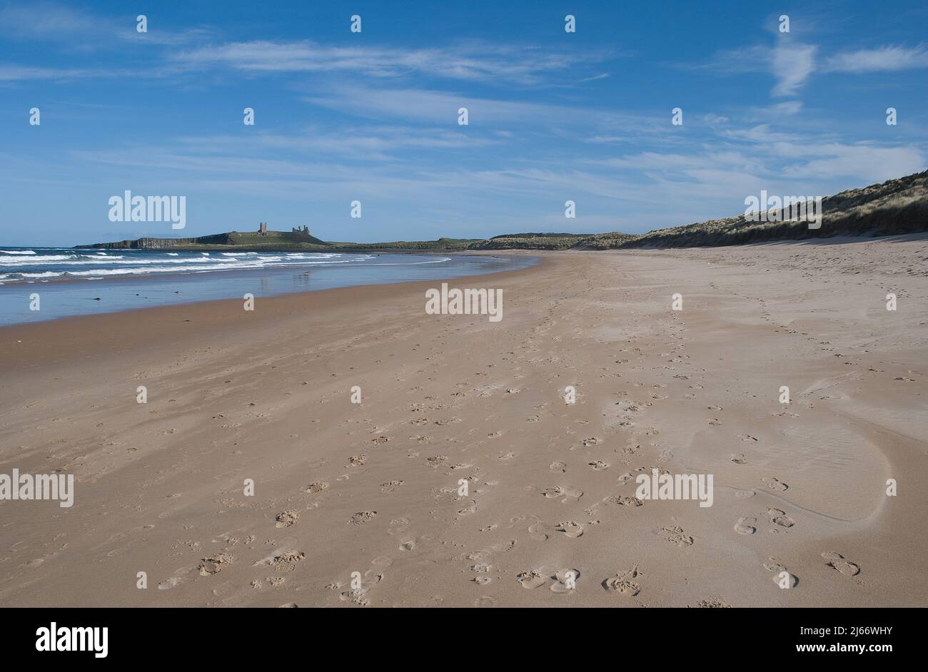 Wide sandy expanse of Embleton Bay in Northumberland curving away with a far distant Dunstanburgh castle on the Whin Sill Stock Photo