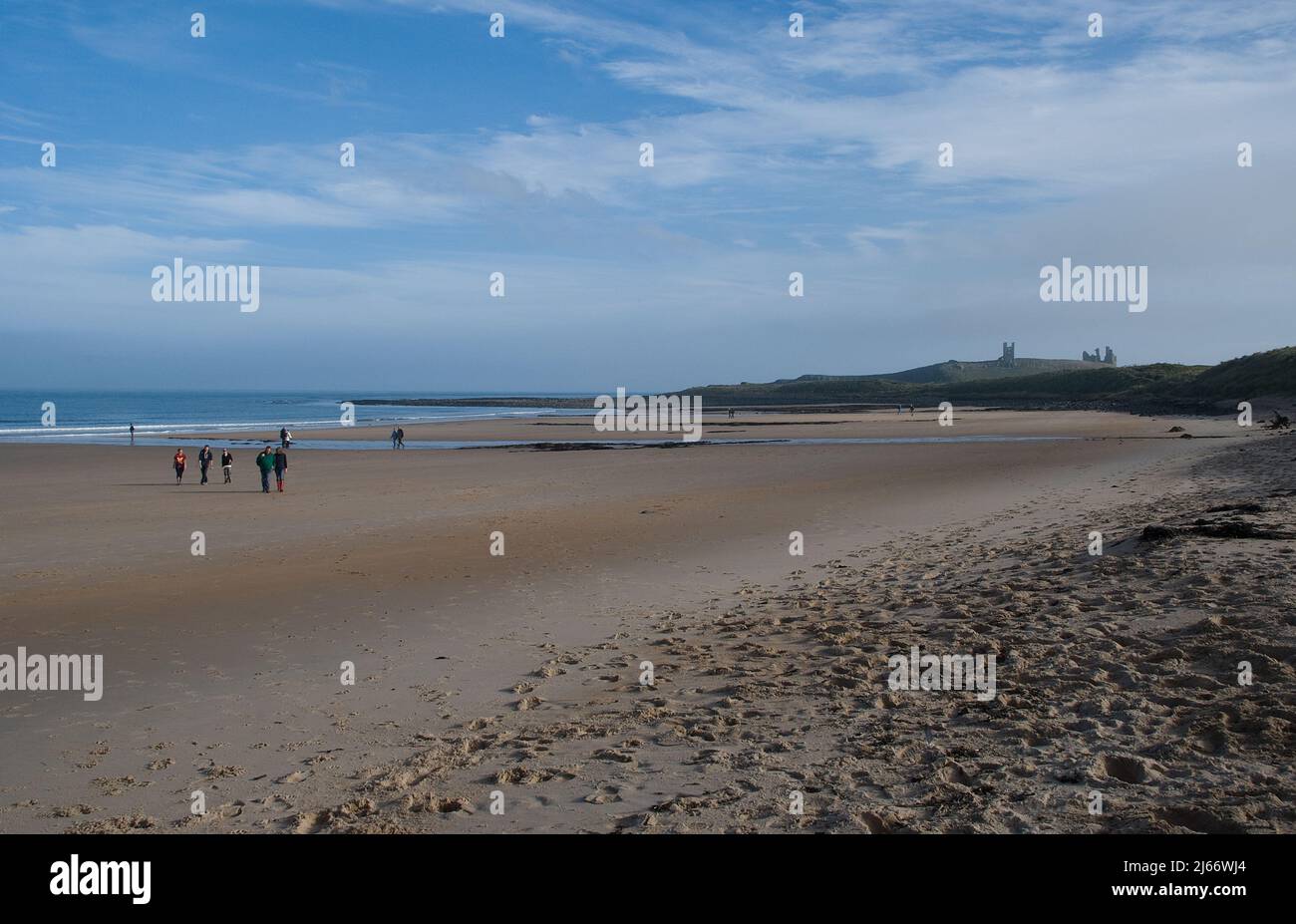 Wide sweeping beach of Embleton Bay with the tide out and a distant Dunstanburgh Castle on the horizon on an autumn afternoon Stock Photo
