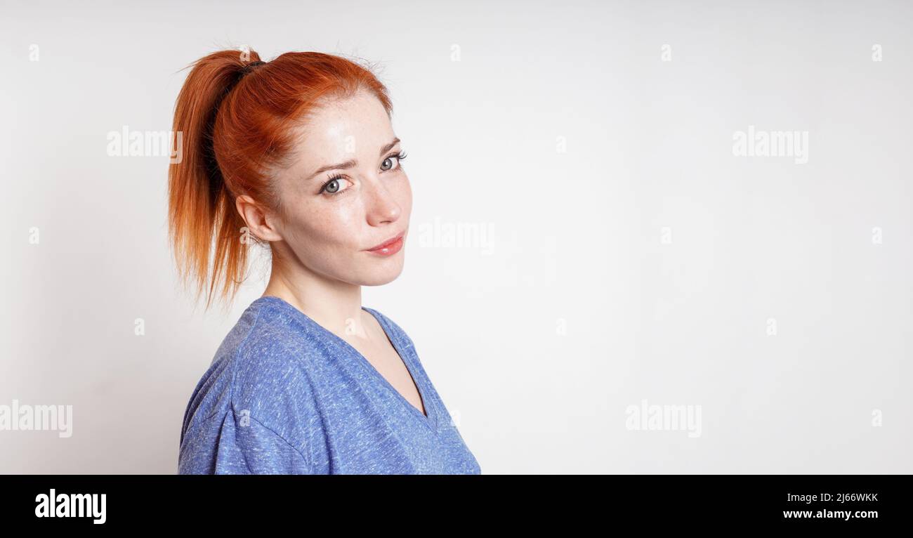 young woman with red hair tied in ponytail tilts her head smiling Stock Photo