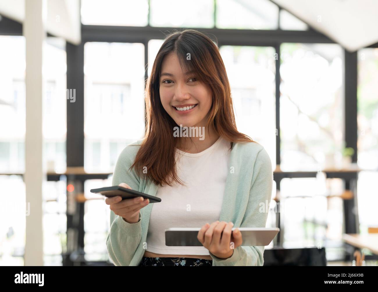Young asian woman using mobile phone and digital tablet looking on camera Stock Photo