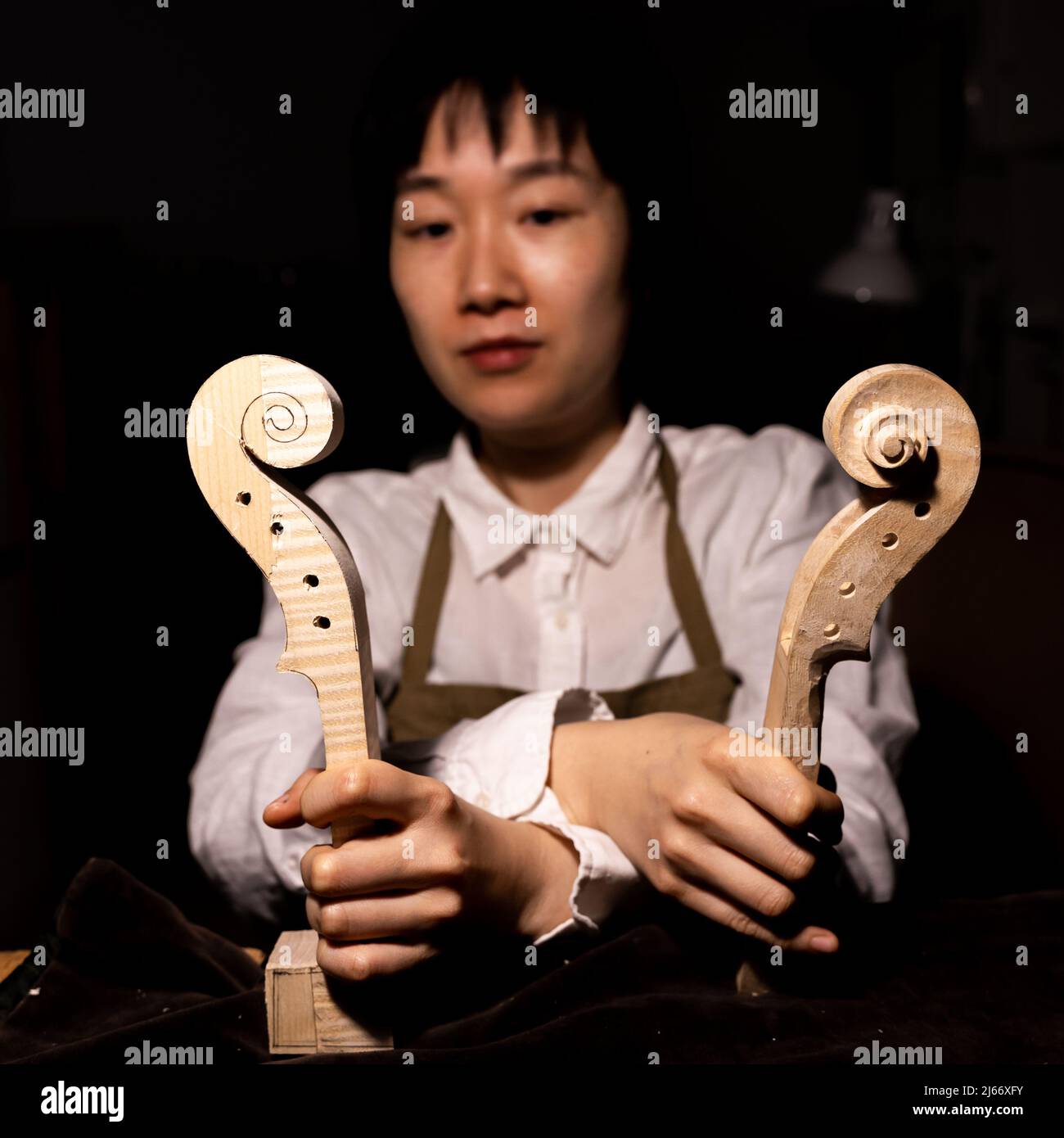 young chinese woman violin maker showing the neck of the violins under construction in her