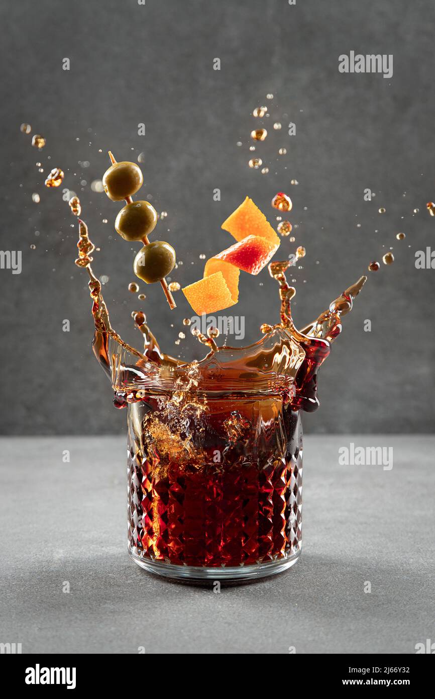 Vermouth cocktail splashing out of glass on light gray background. Vertical format. Stock Photo