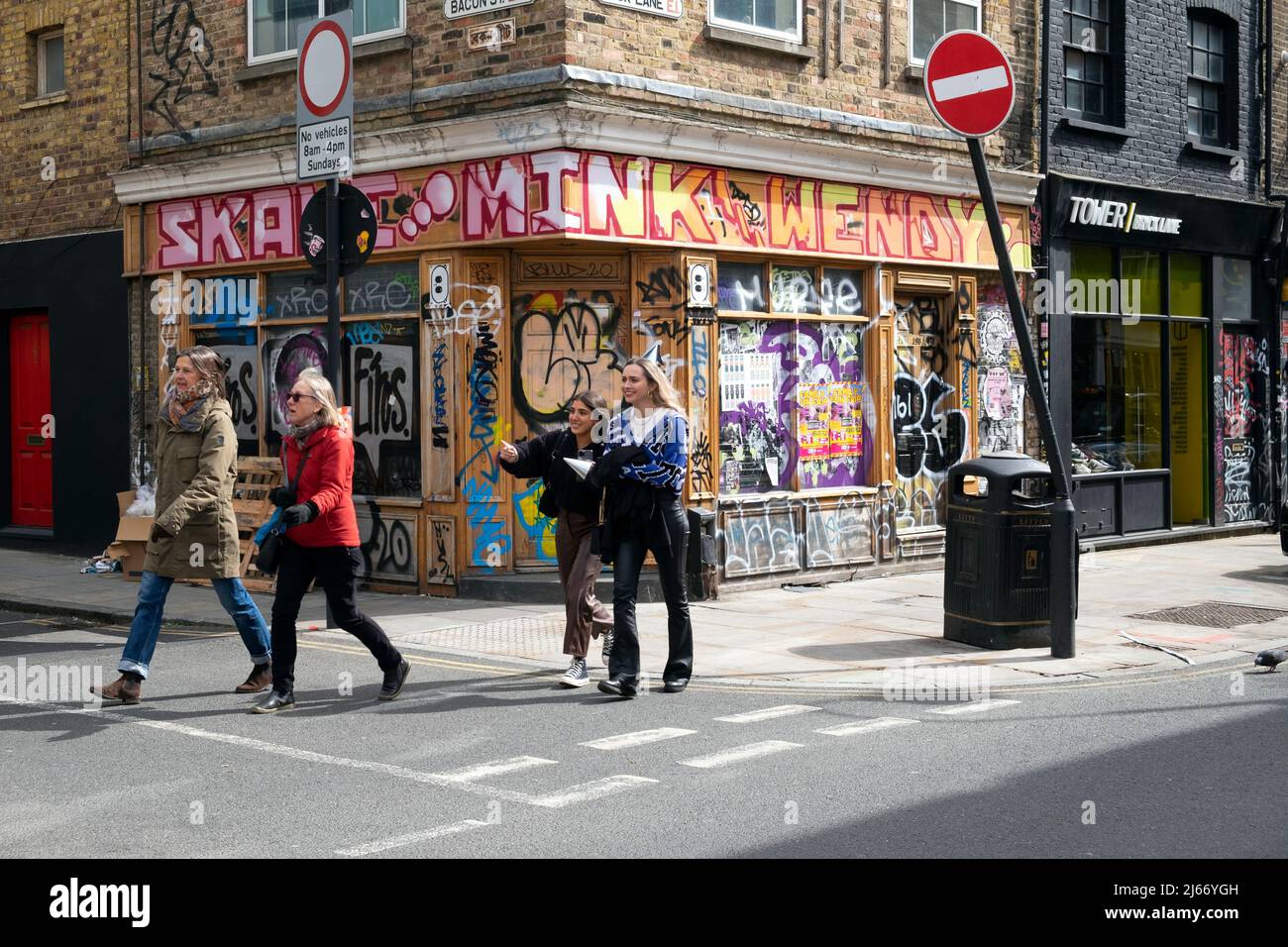 People walking along Brick Lane on the corner of Bacon Street past a closed shop covered in graffiti in East London E1 England UK  KATHY DEWITT Stock Photo