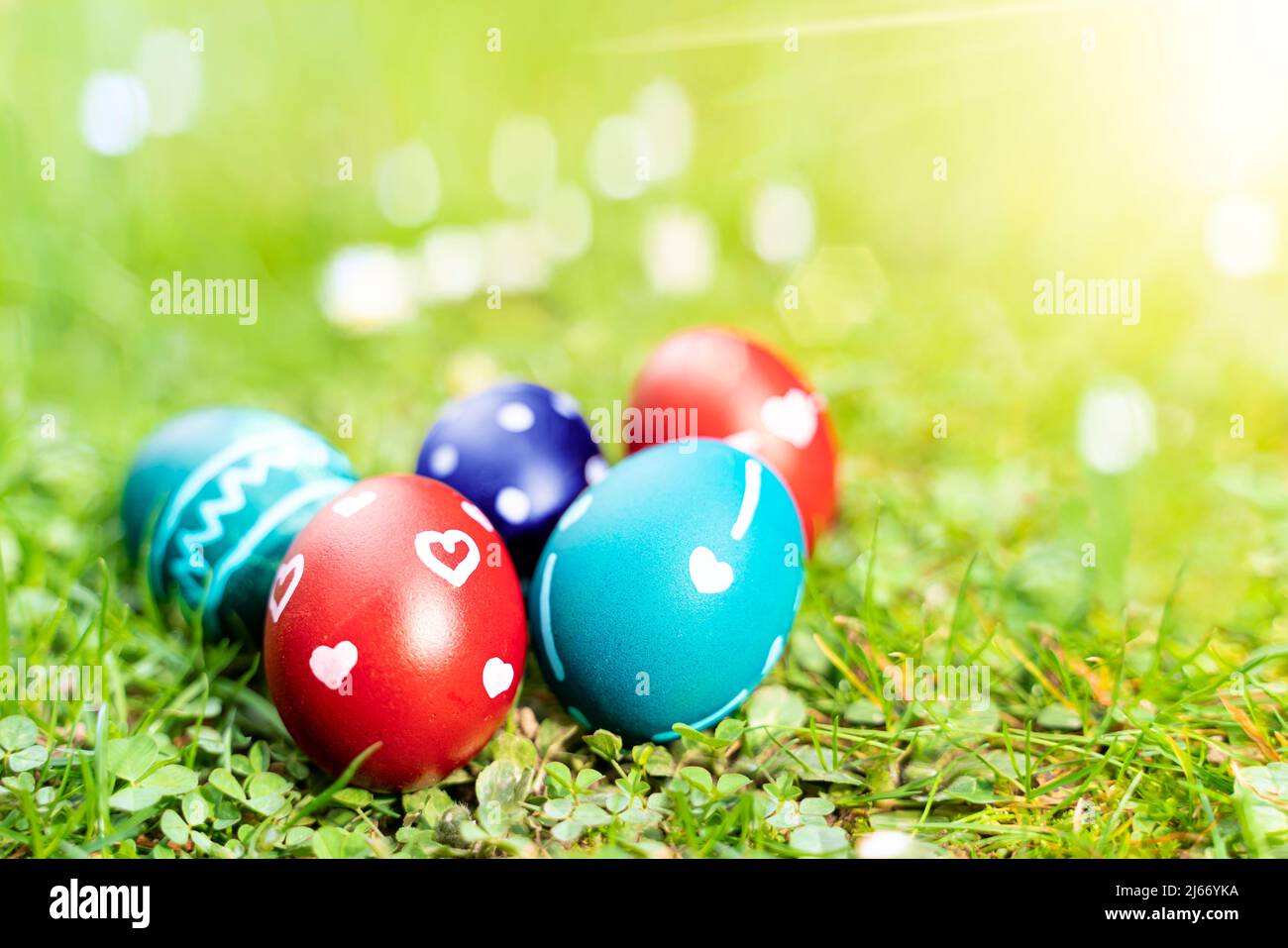 Beautiful painted real easter eggs lie in the fresh spring grass. The sun is shining. Red and turquoise eggs are decorated with white ornaments. Stock Photo
