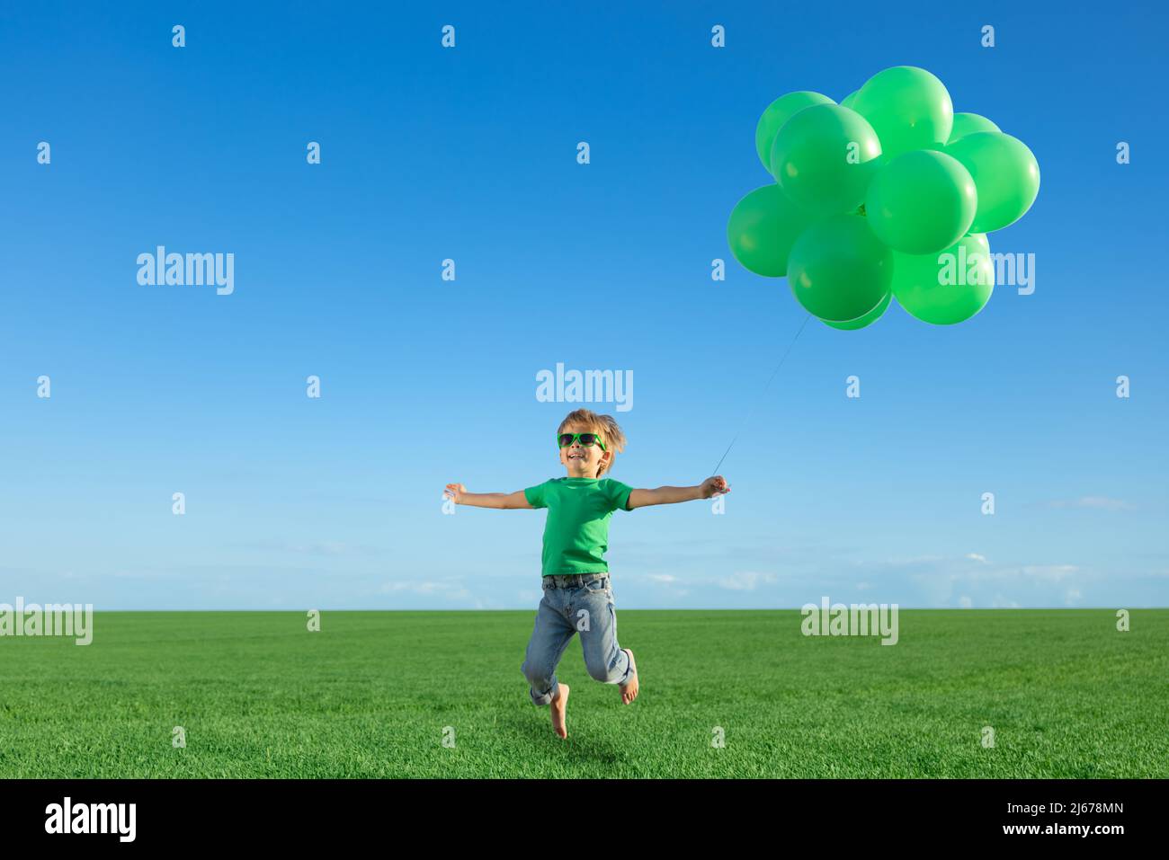 Happy child playing with bright multicolor balloons outdoor. Kid having fun in green spring field against blue sky background. Healthy and active life Stock Photo