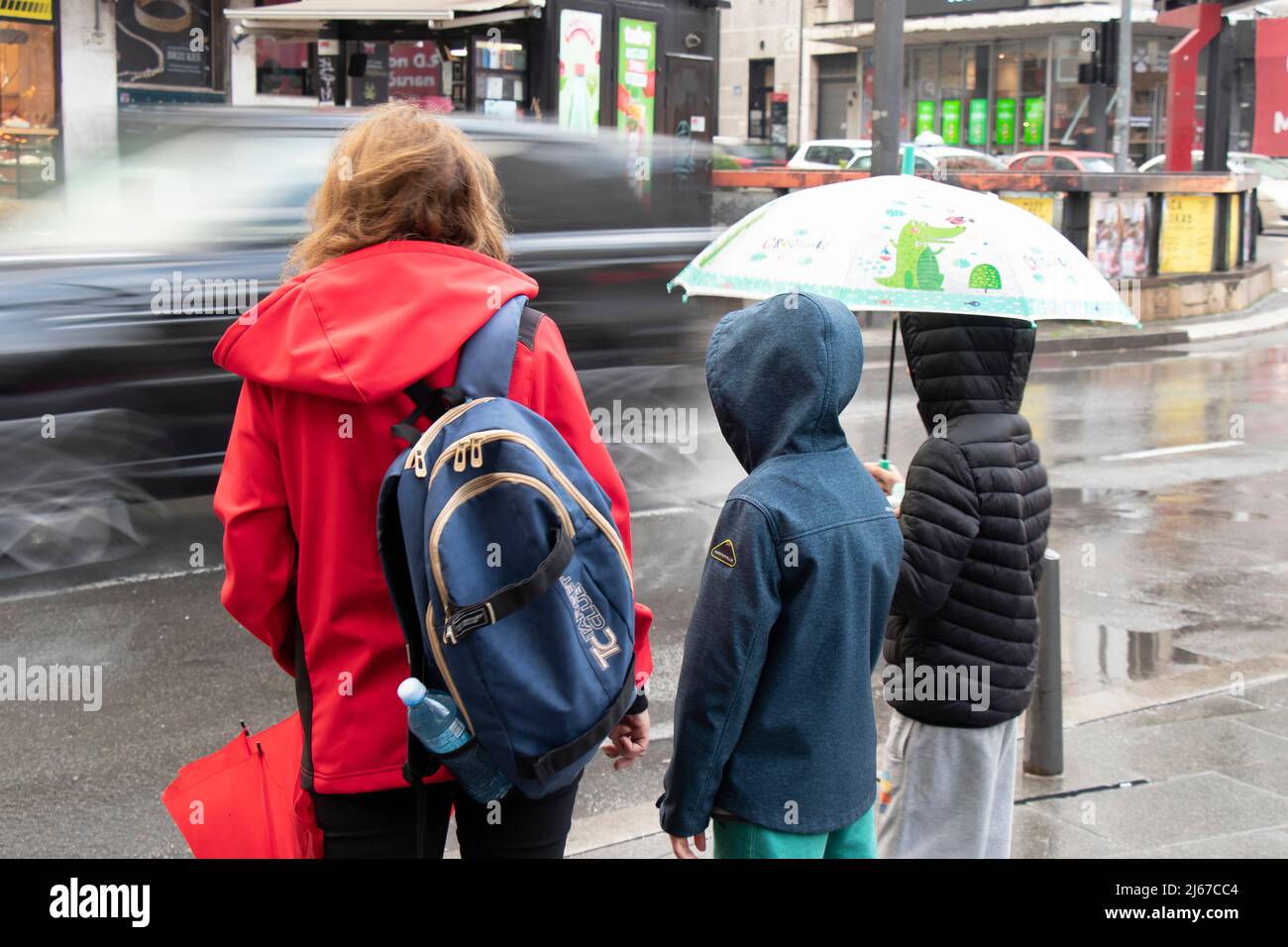 Belgrade, Serbia - April 27, 2022: Mother walking children to school and waiting at crossroad on a rainy day Stock Photo