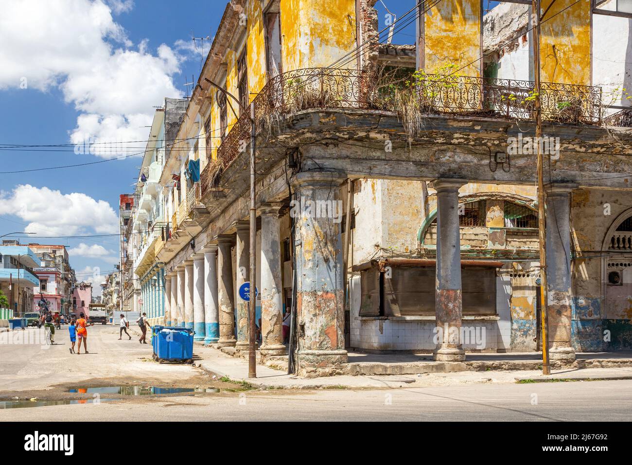 Collapsed run-down building in a street corner. There are children playing in the residential district of the Cuban capital city.  Dirty water puddles Stock Photo