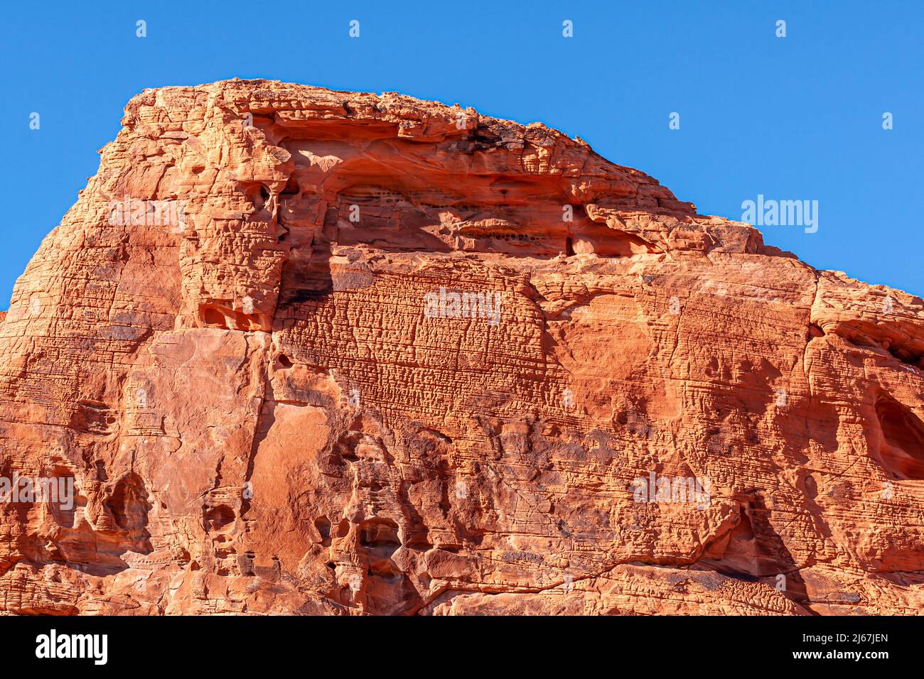 Overton, Nevada, USA - February 24, 2010: Valley of Fire. Lines of ancient script like natural carvings in flank of red rock mountain under blue sky. Stock Photo