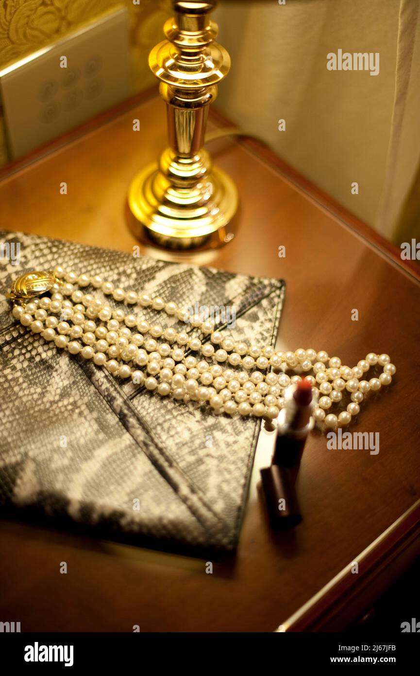 Hotel room night table with jewellery lipstick and woman purse. Stock Photo