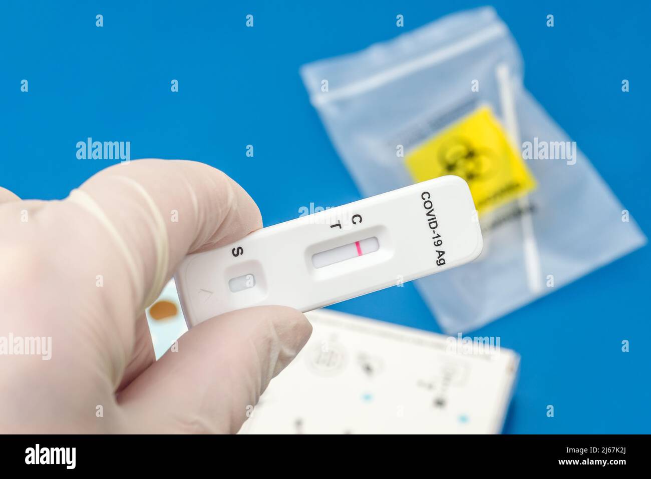 Gloved hand holding a SARS-Cov-2 antigen test strip showing a negative result. A nasal swab inside a bag is visible in background. Stock Photo