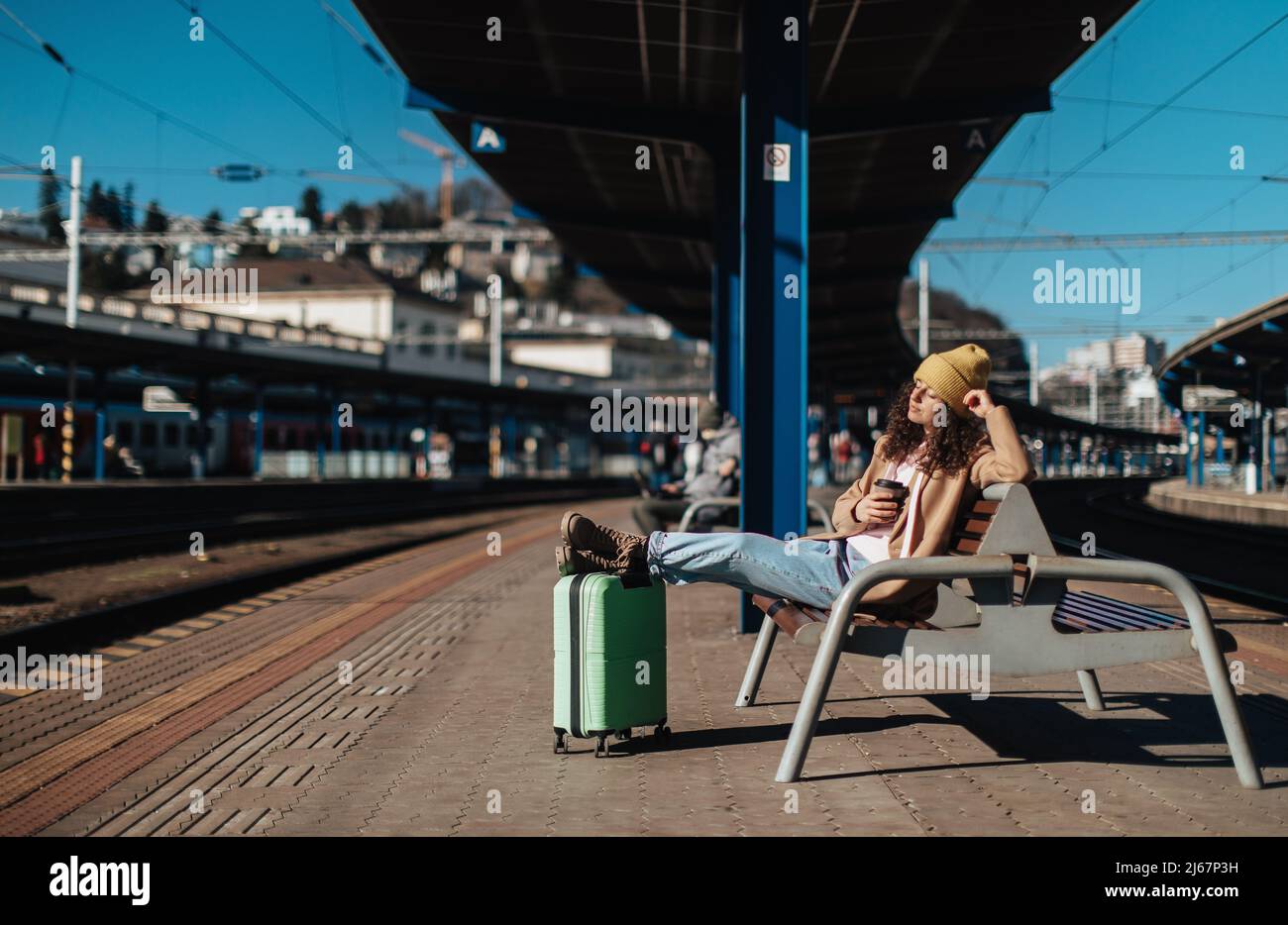 Young traveler woman sitting alone at train station platform with luggage. Stock Photo