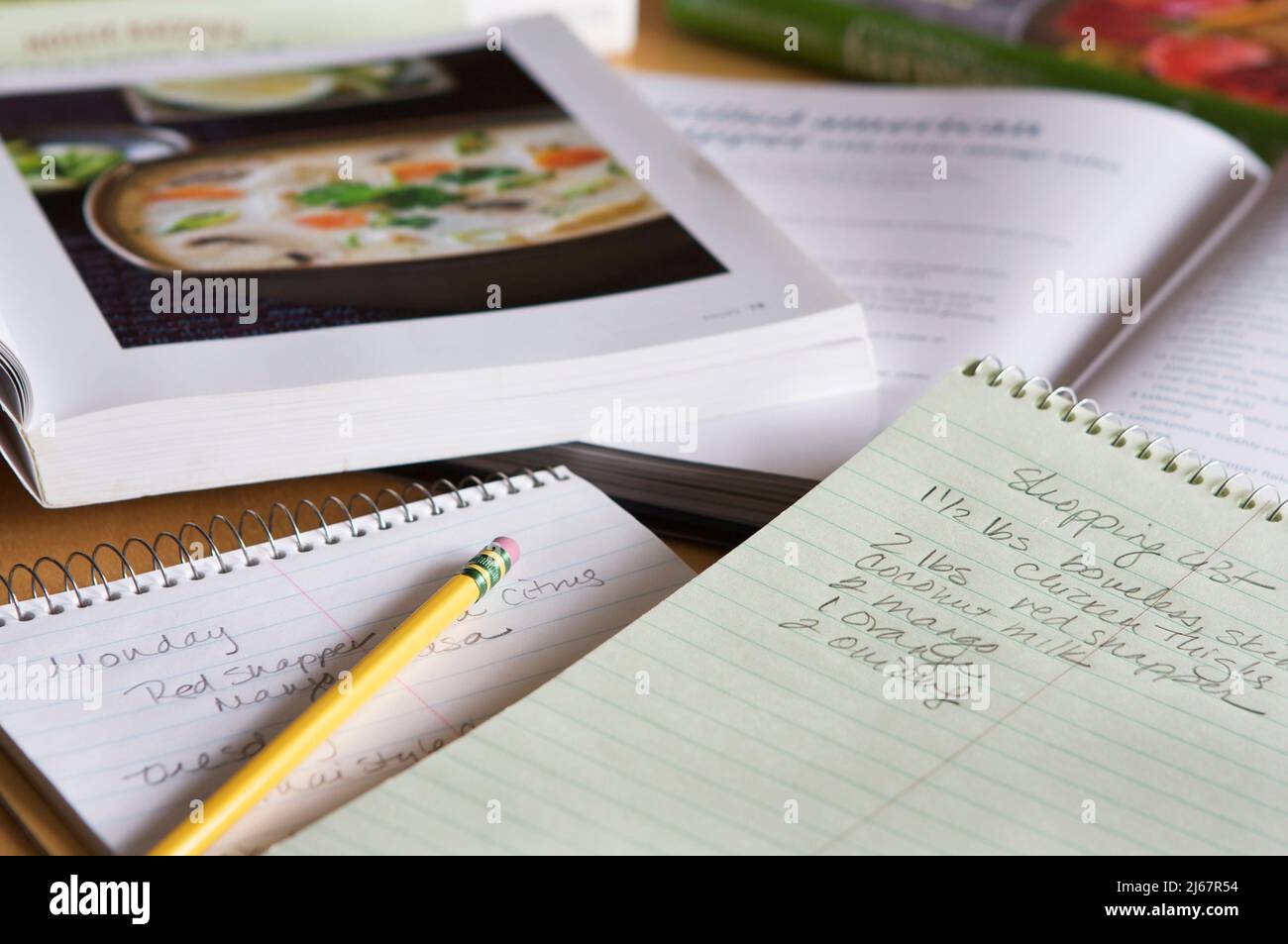 Open cookbooks, pencil, and handwritten lists for shopping and meal planning spread on a table in natural light. Stock Photo