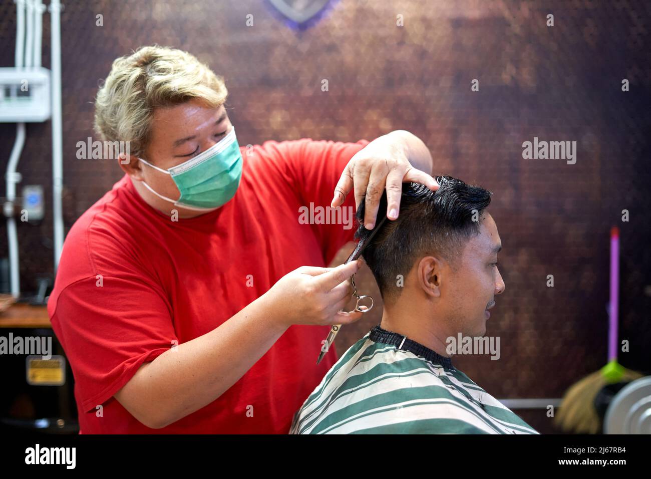 Barber wearing mask cutting the hair of a client using scissors and