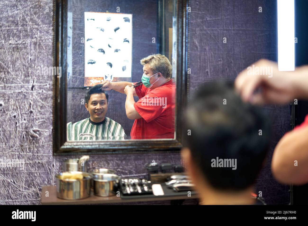 Mirror image of a barber cutting a customer's hair Stock Photo