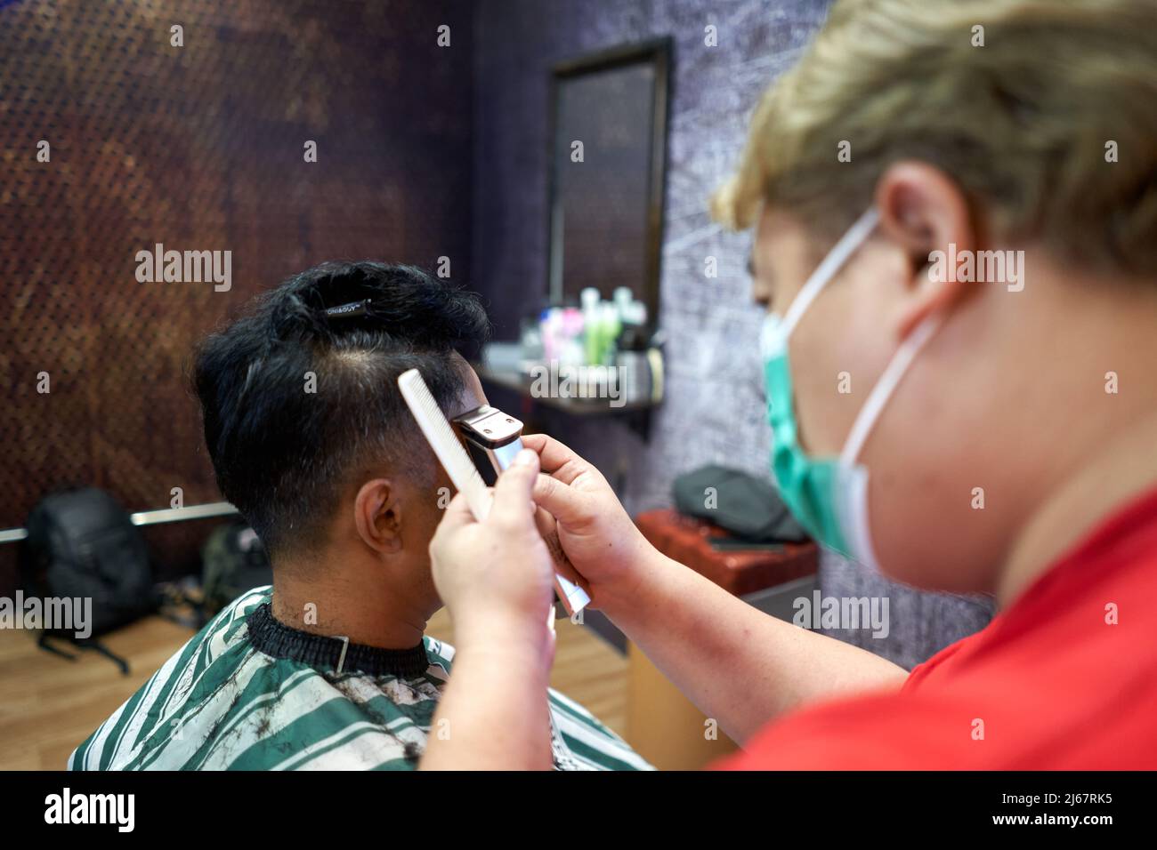 Barber cutting the hair on the side of the head of a customer in a